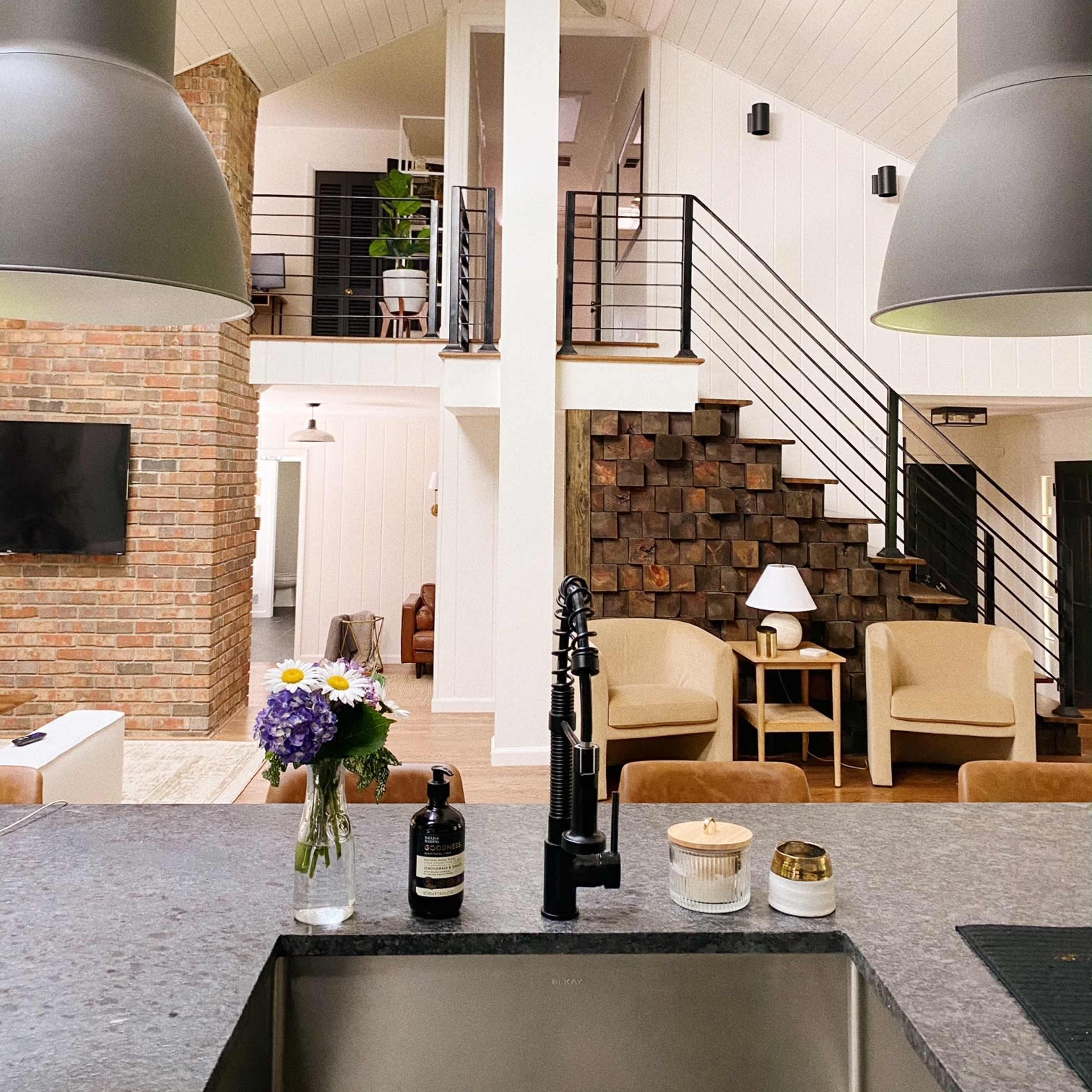 A modern open-concept living space with high ceilings, a kitchen island, and a staircase leading to a loft area.