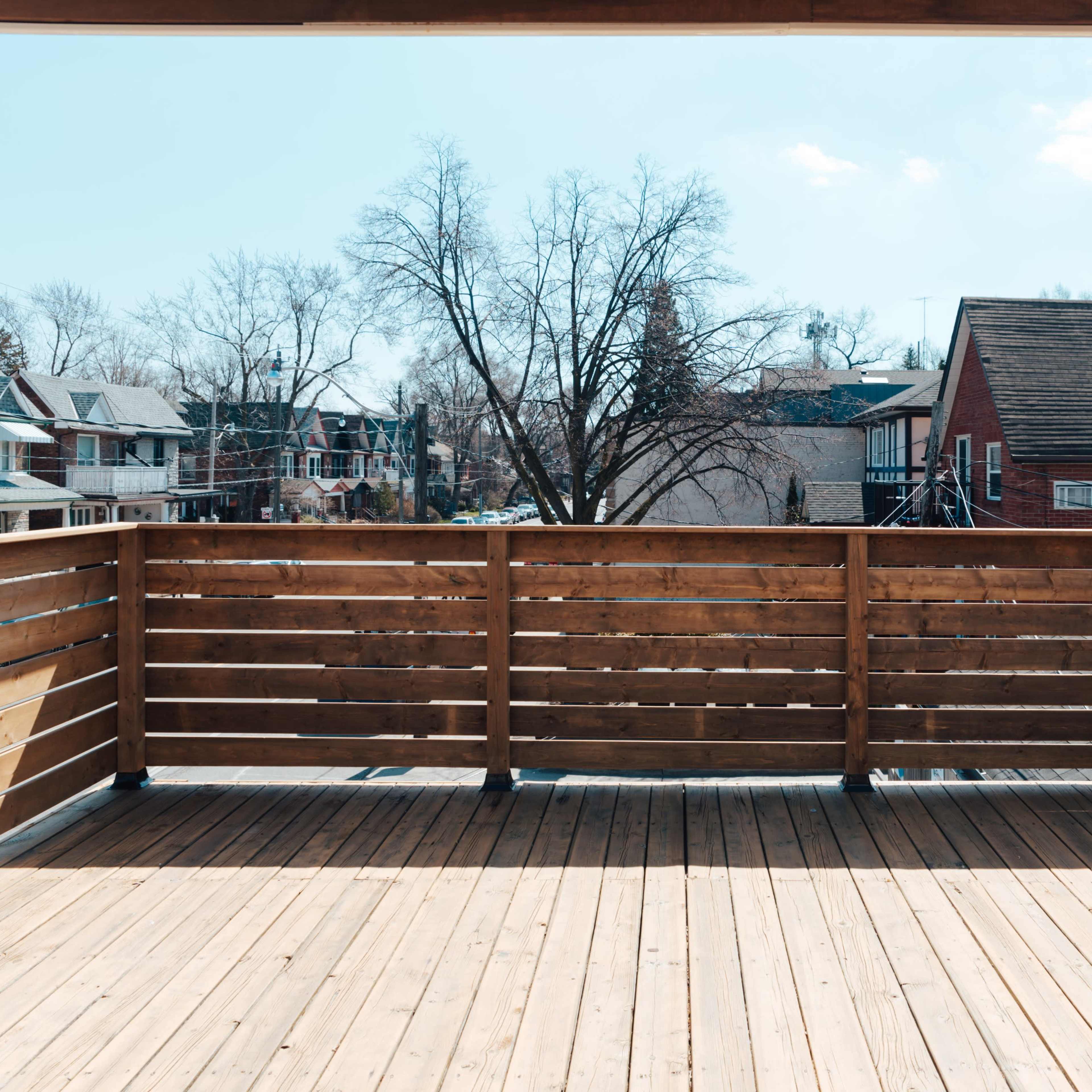 A wooden deck overlooks a neighborhood with houses and bare trees under a clear sky.