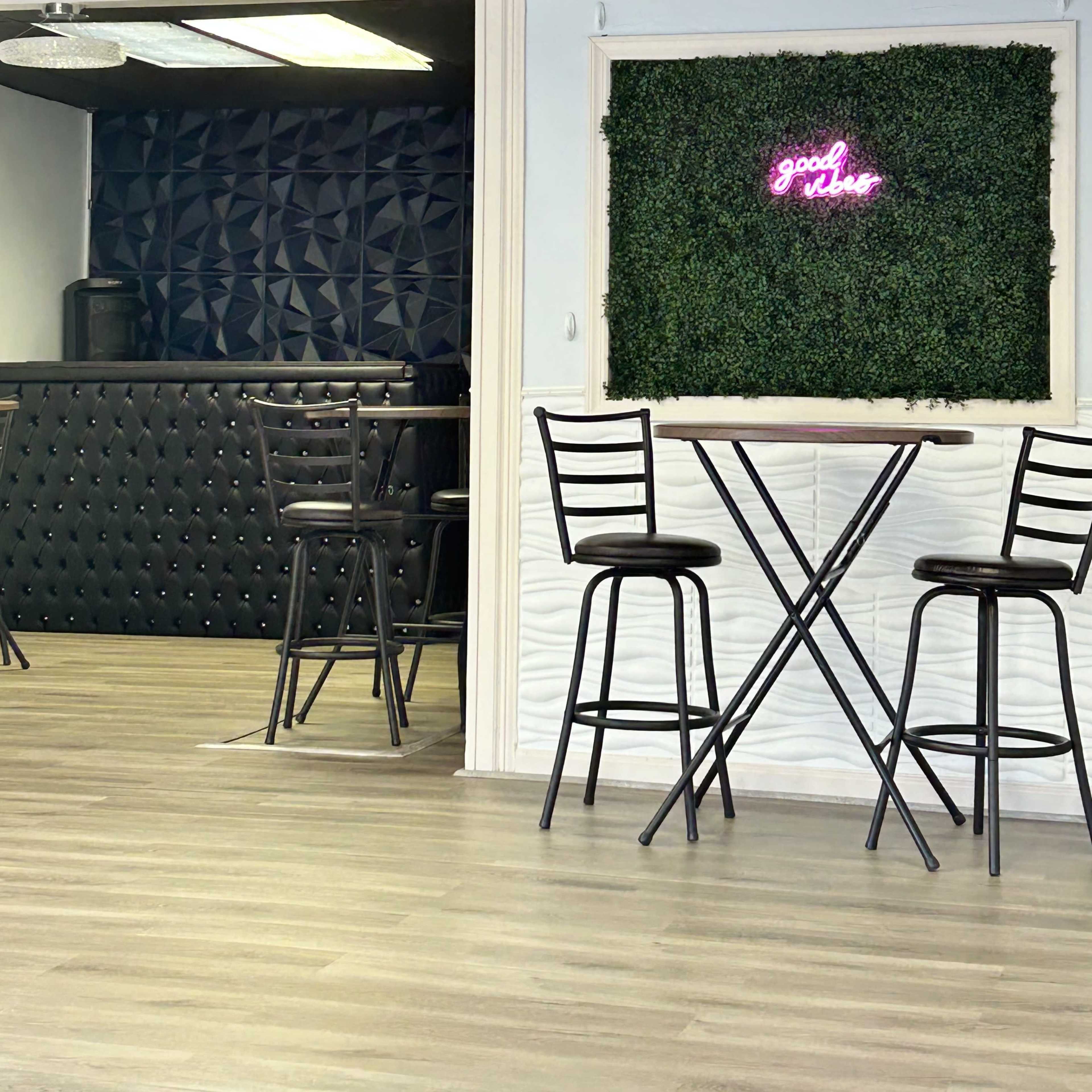 A modern interior with a bar area featuring a textured black wall, two tall bar stools, and a neon sign on a green wall that reads "good vibes."