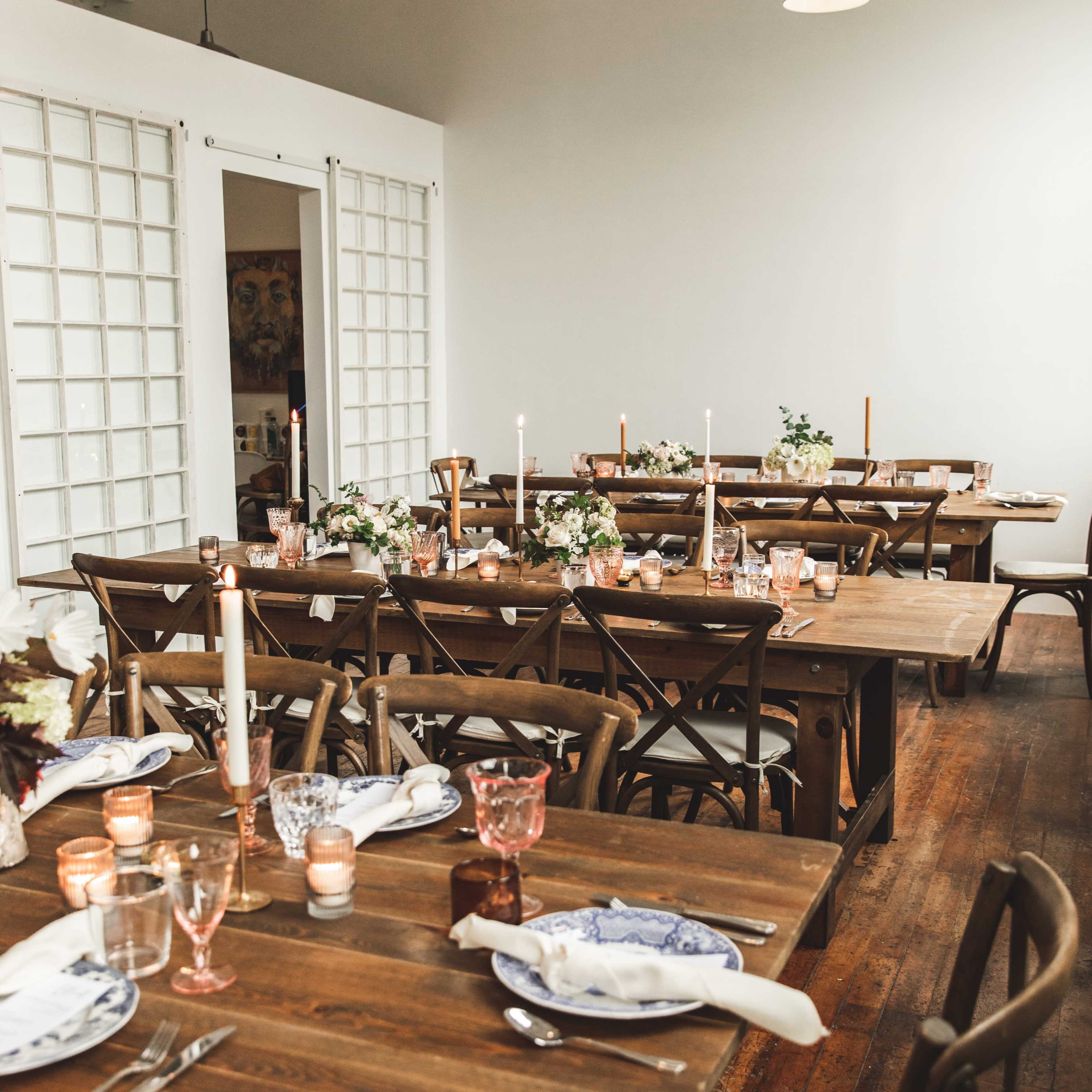A dining area with wooden tables set for a meal, featuring candles and floral arrangements.
