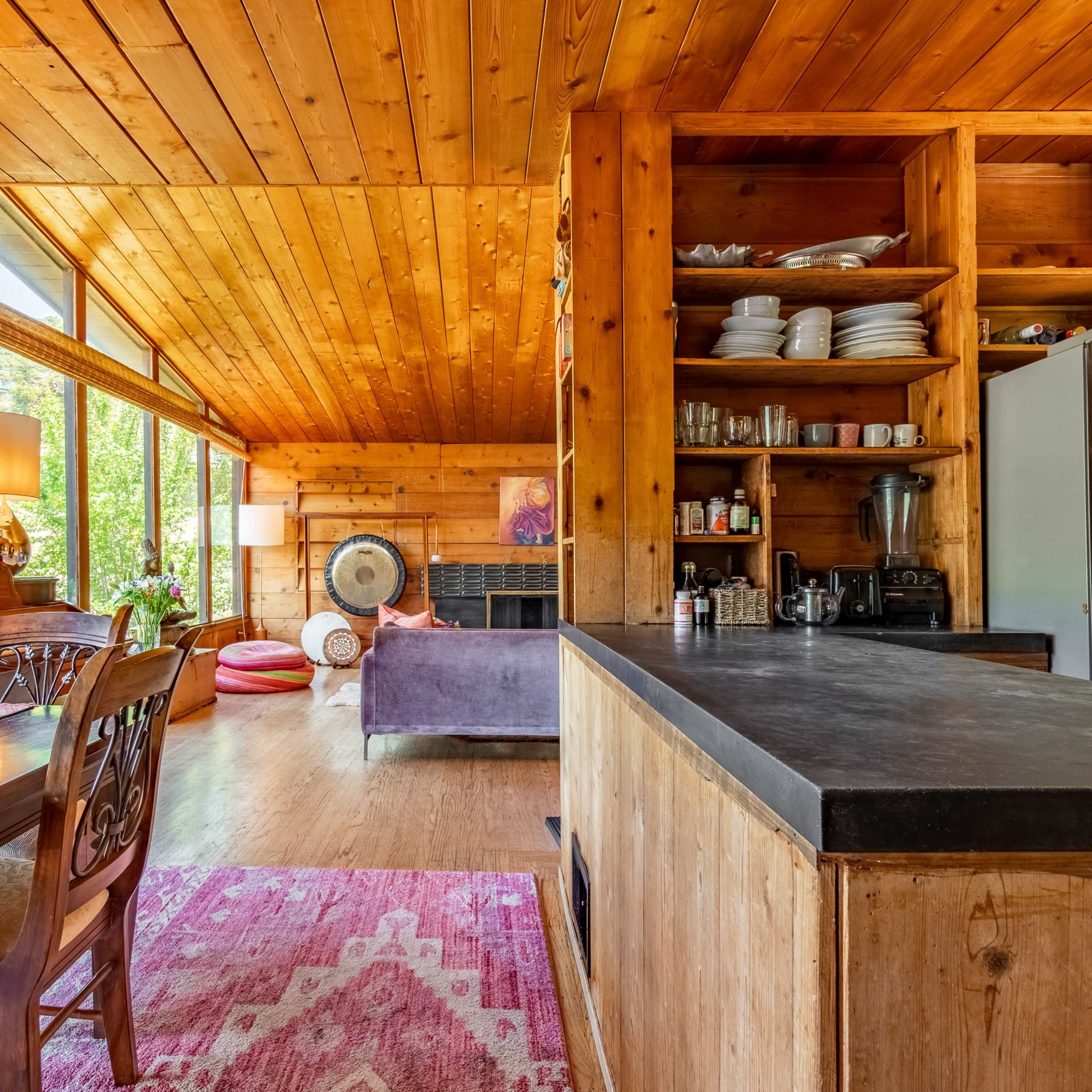 A warm, wooden kitchen with an island, stainless steel appliances, and open shelving displaying dishes and jars.