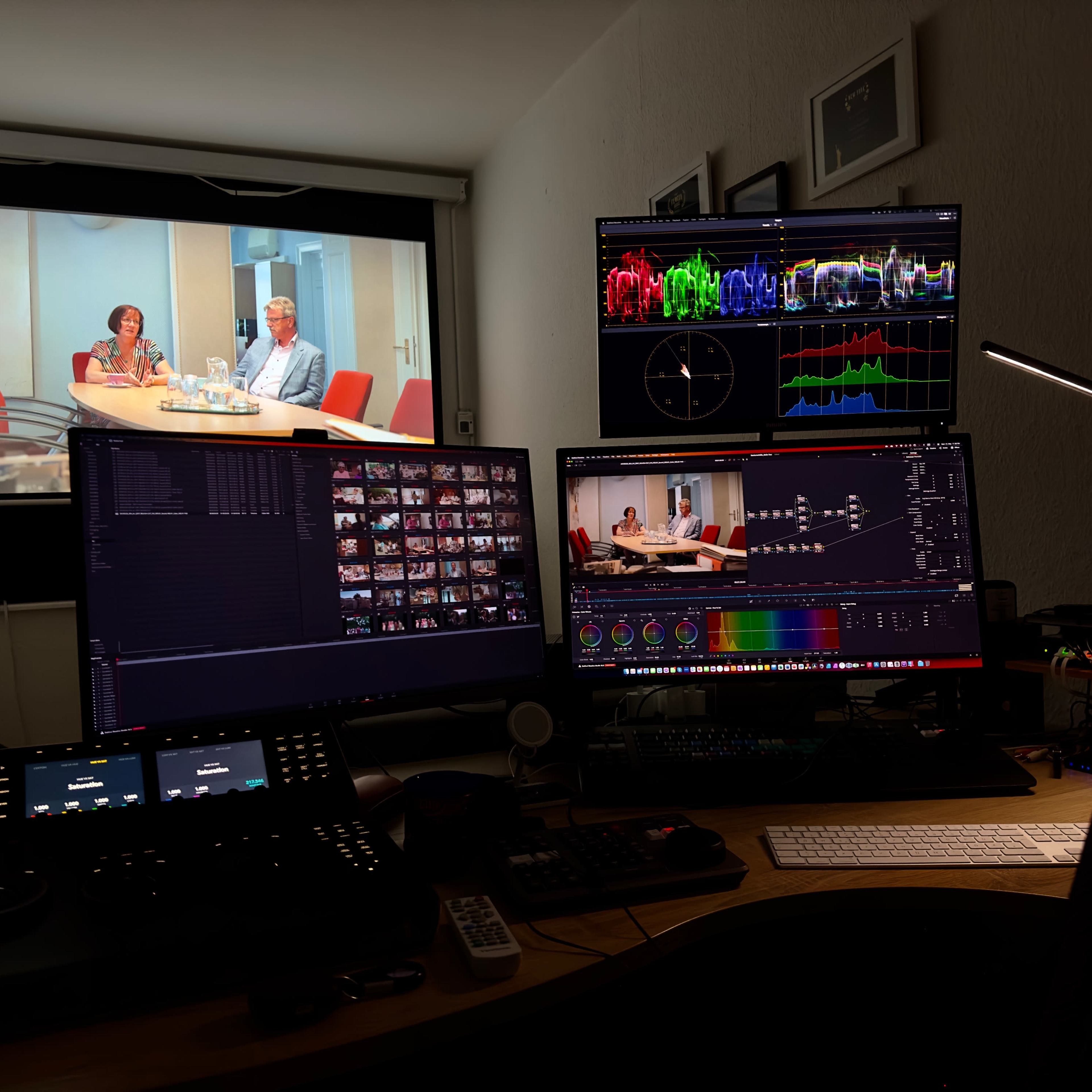 A video editing setup with multiple monitors displaying a video interview and various editing tools.