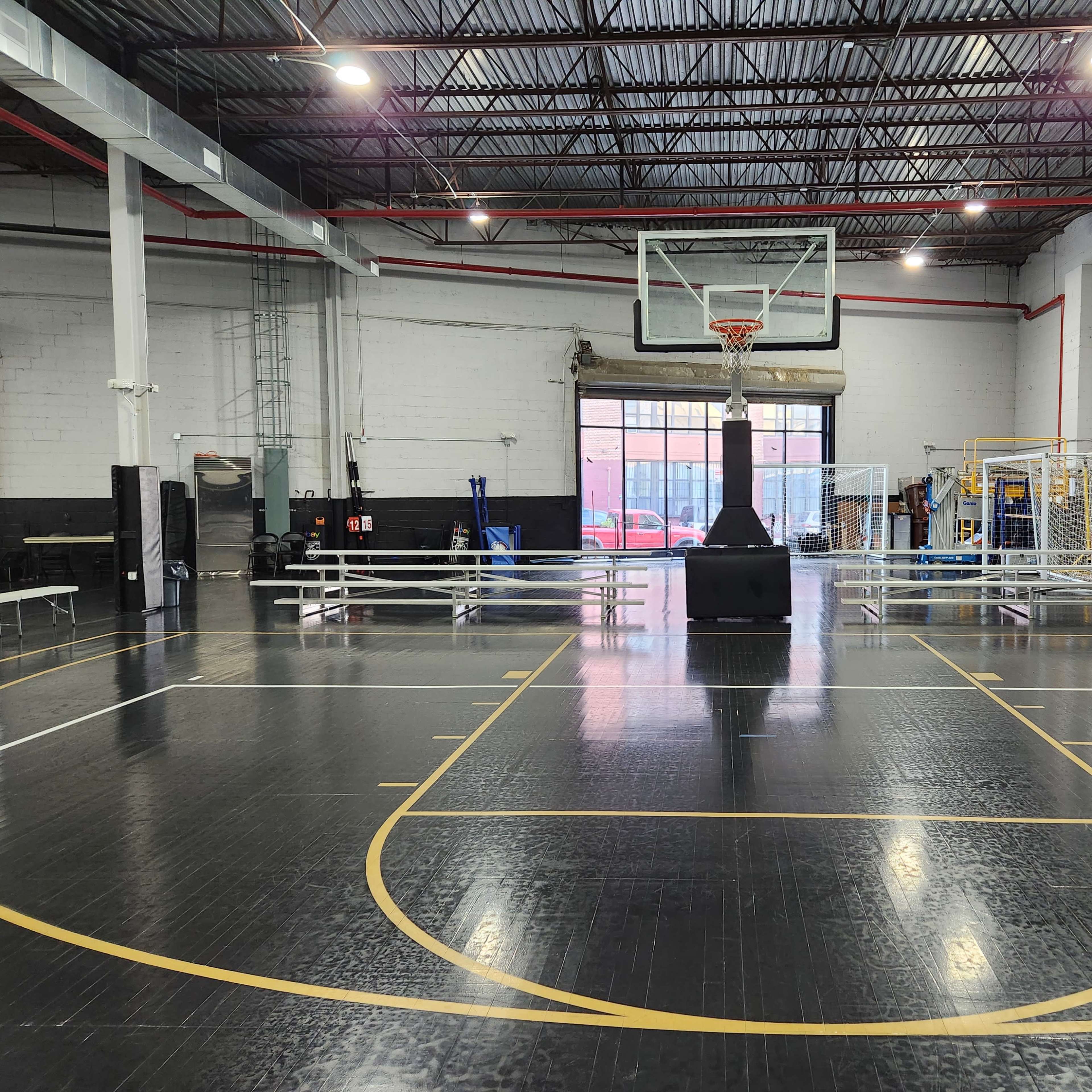 A basketball court with a hoop at the far end, surrounded by benches and equipment in a well-lit indoor gymnasium.