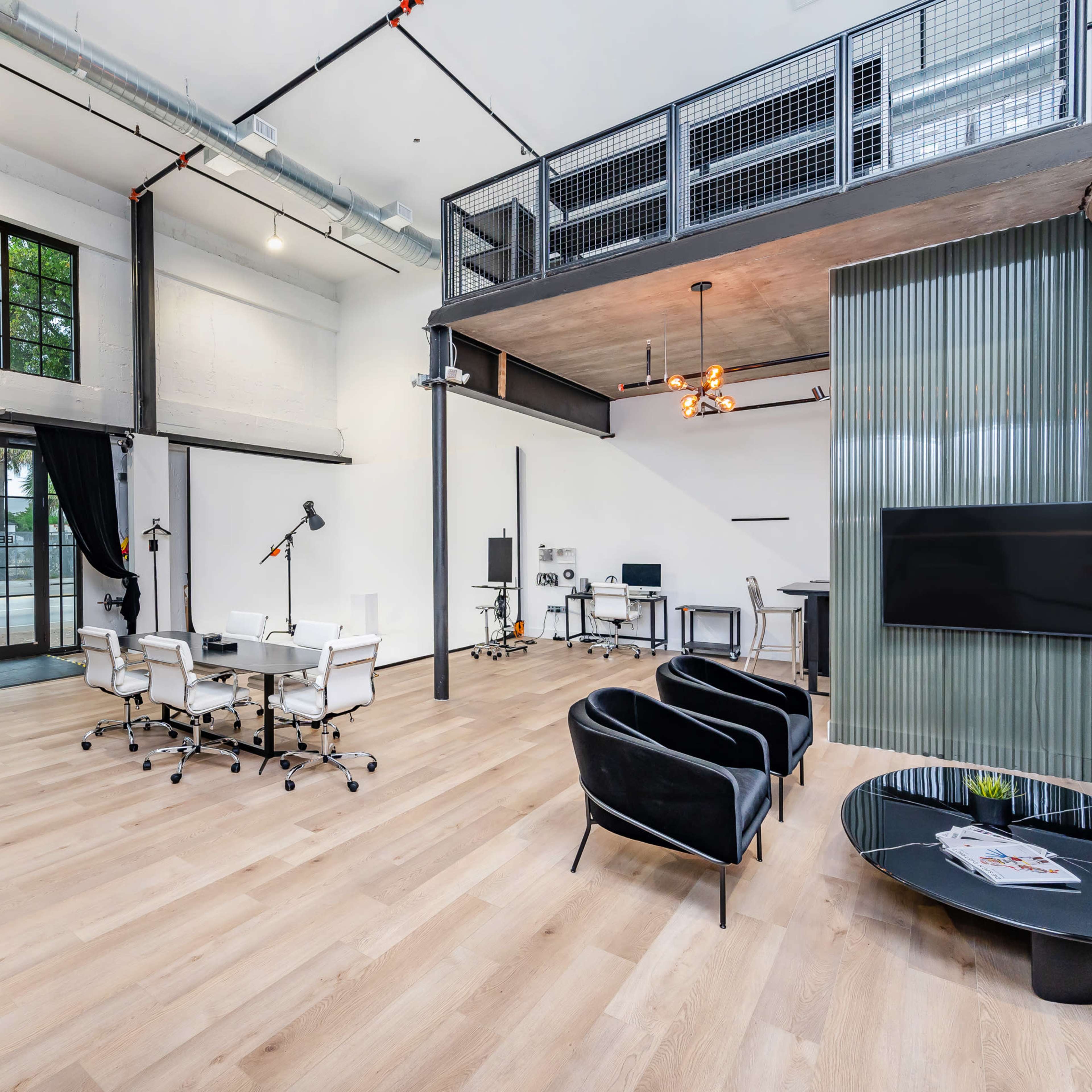 An open-concept workspace featuring modern furniture, large windows, and a mezzanine level.