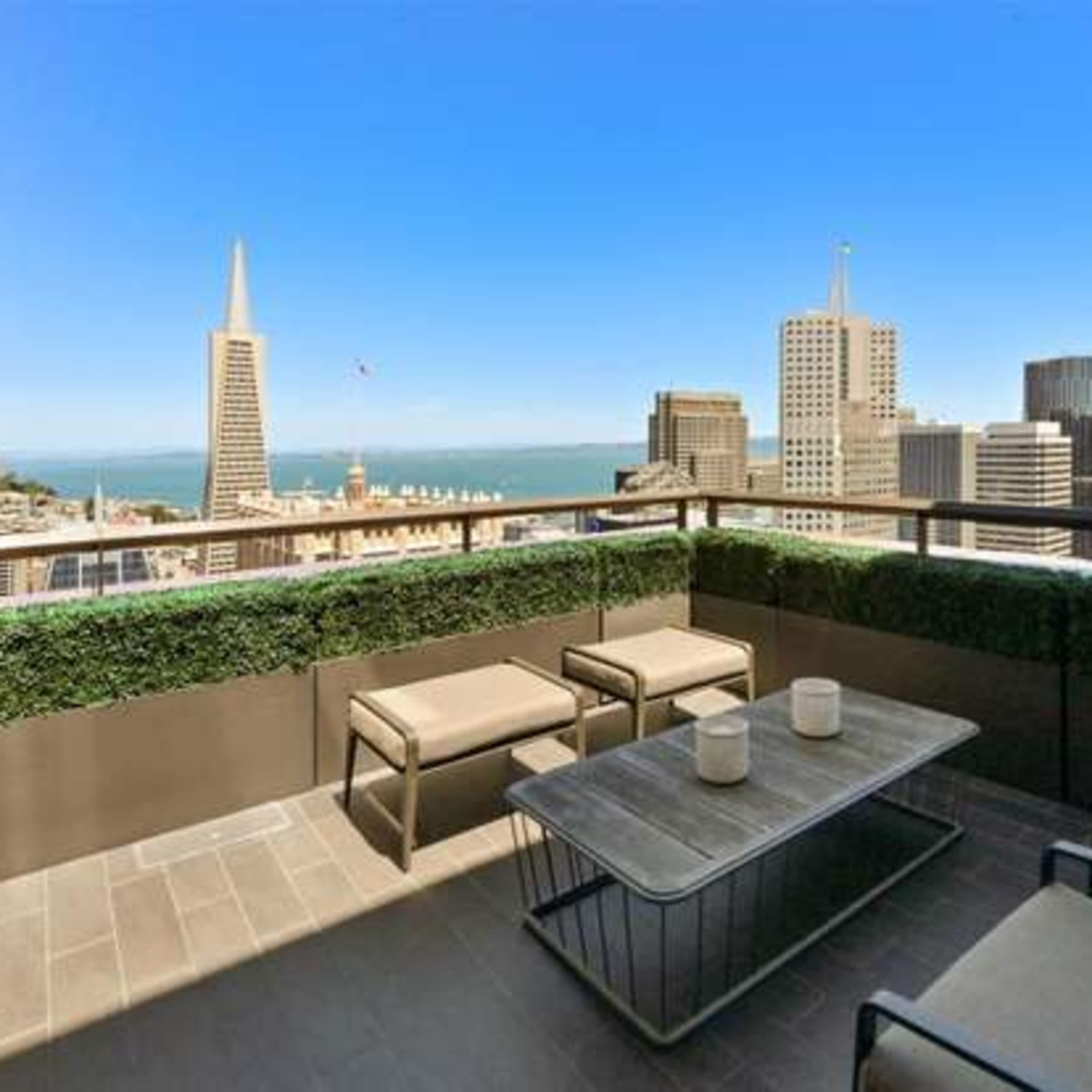 A balcony with modern furniture overlooking a skyline that includes the Transamerica Pyramid in San Francisco.