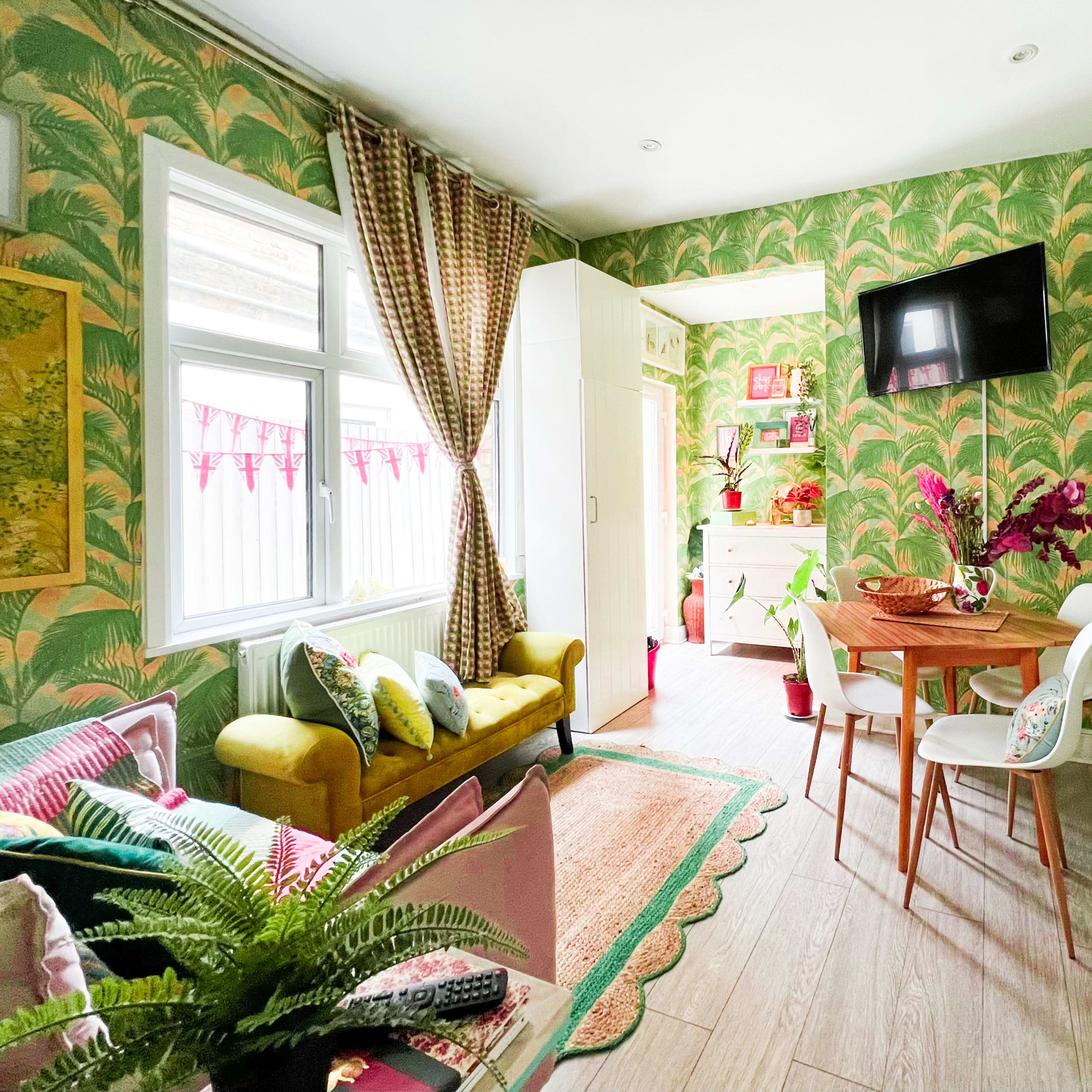 A small, brightly decorated kitchen and dining area with green floral wallpaper, a round dining table, and a cozy seating arrangement.