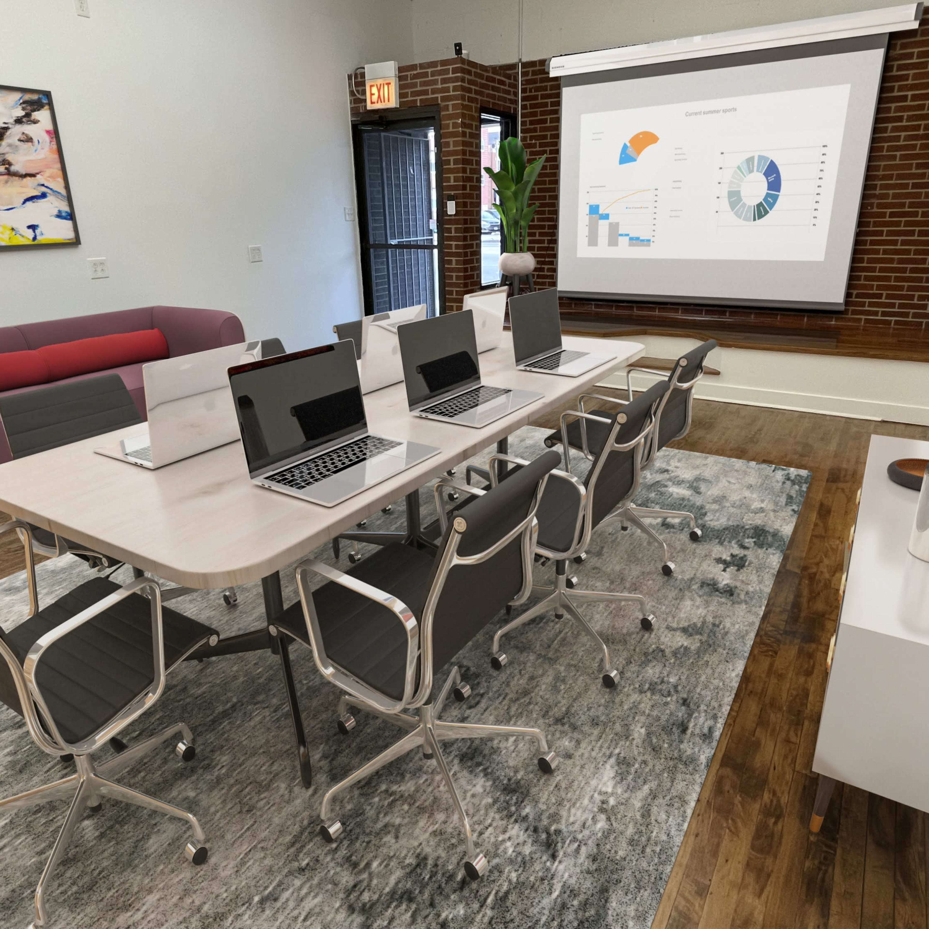 A modern conference room features a long table with multiple laptops, a large screen displaying graphs, and contemporary decor, including artwork and plants.