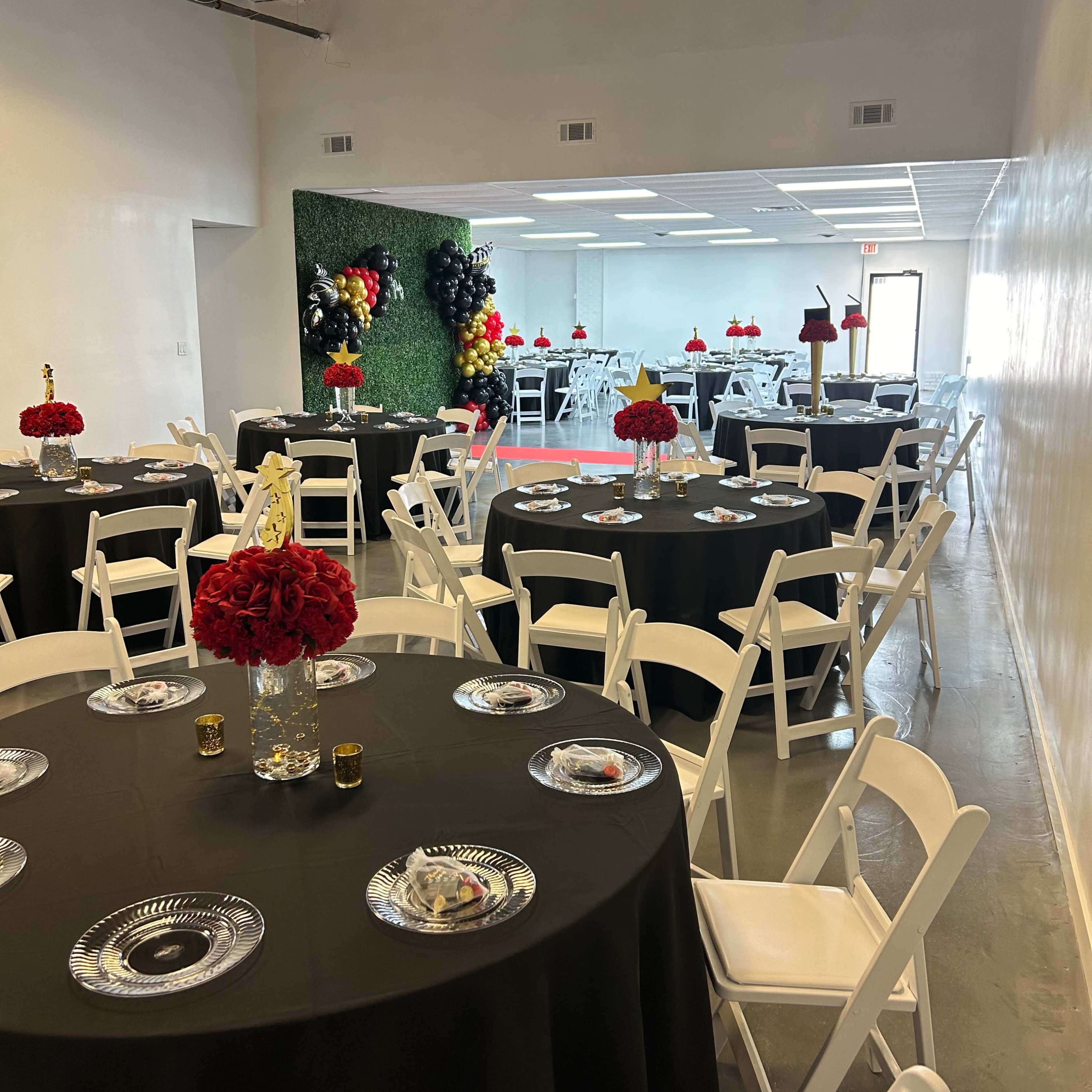 A banquet hall set up with black tablecloths, white chairs, and centerpieces of red flowers, ready for an event.
