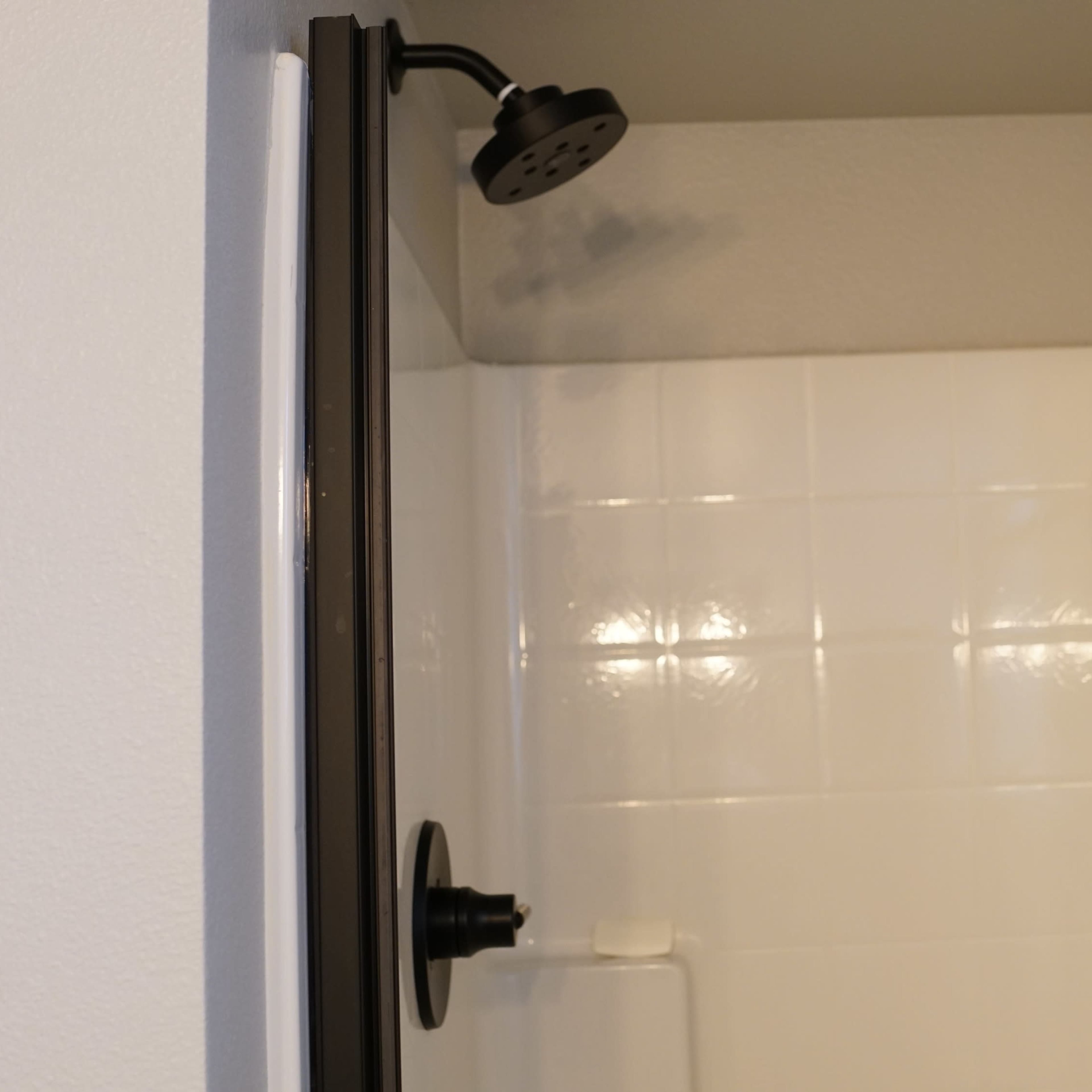 A modern shower stall with a black showerhead and two bottles of shampoo and conditioner on a white tiled shelf.