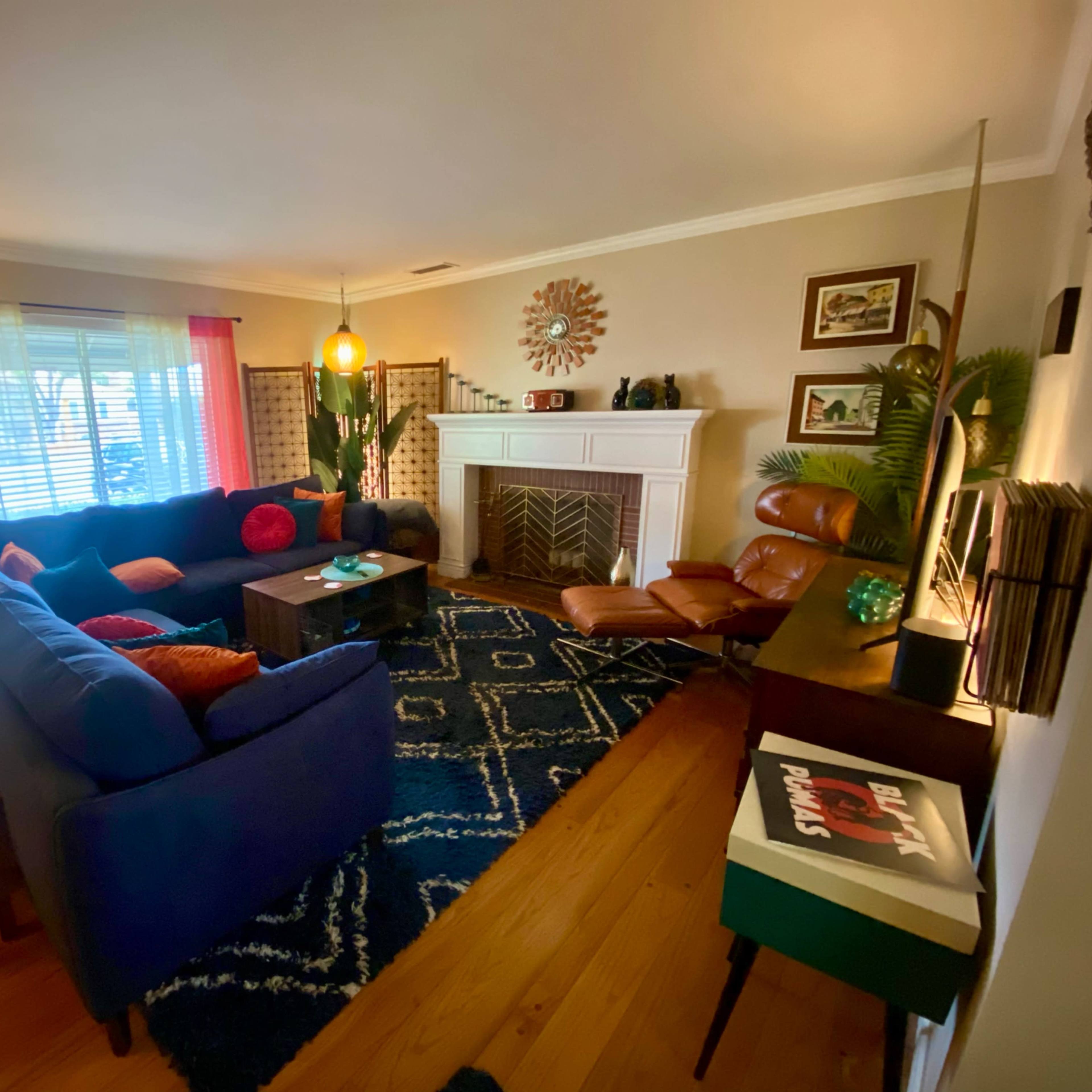 A living room with a blue sectional sofa, a fireplace, a wooden floor, and decorative plants.