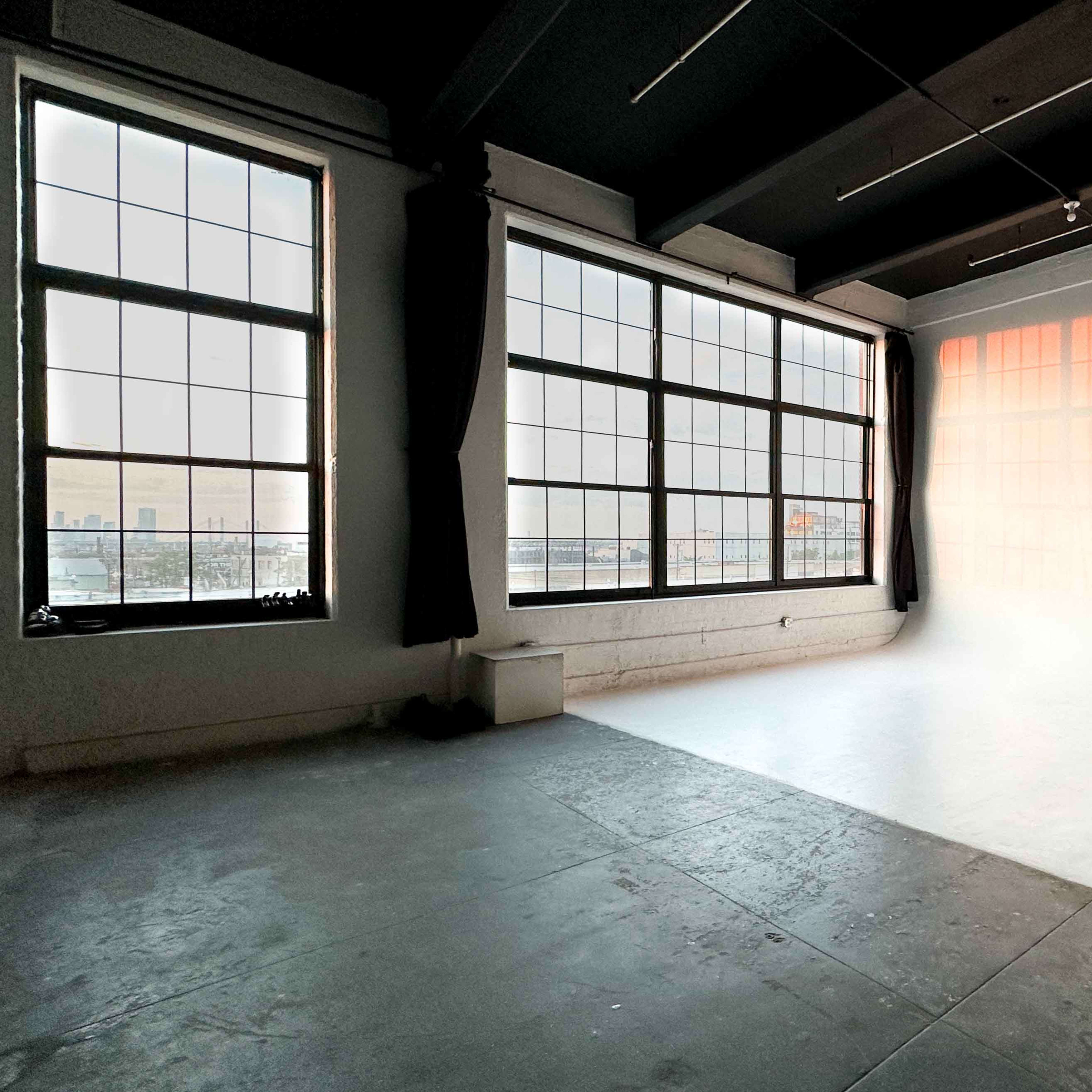 A spacious, well-lit interior room with large windows and a plain white wall.