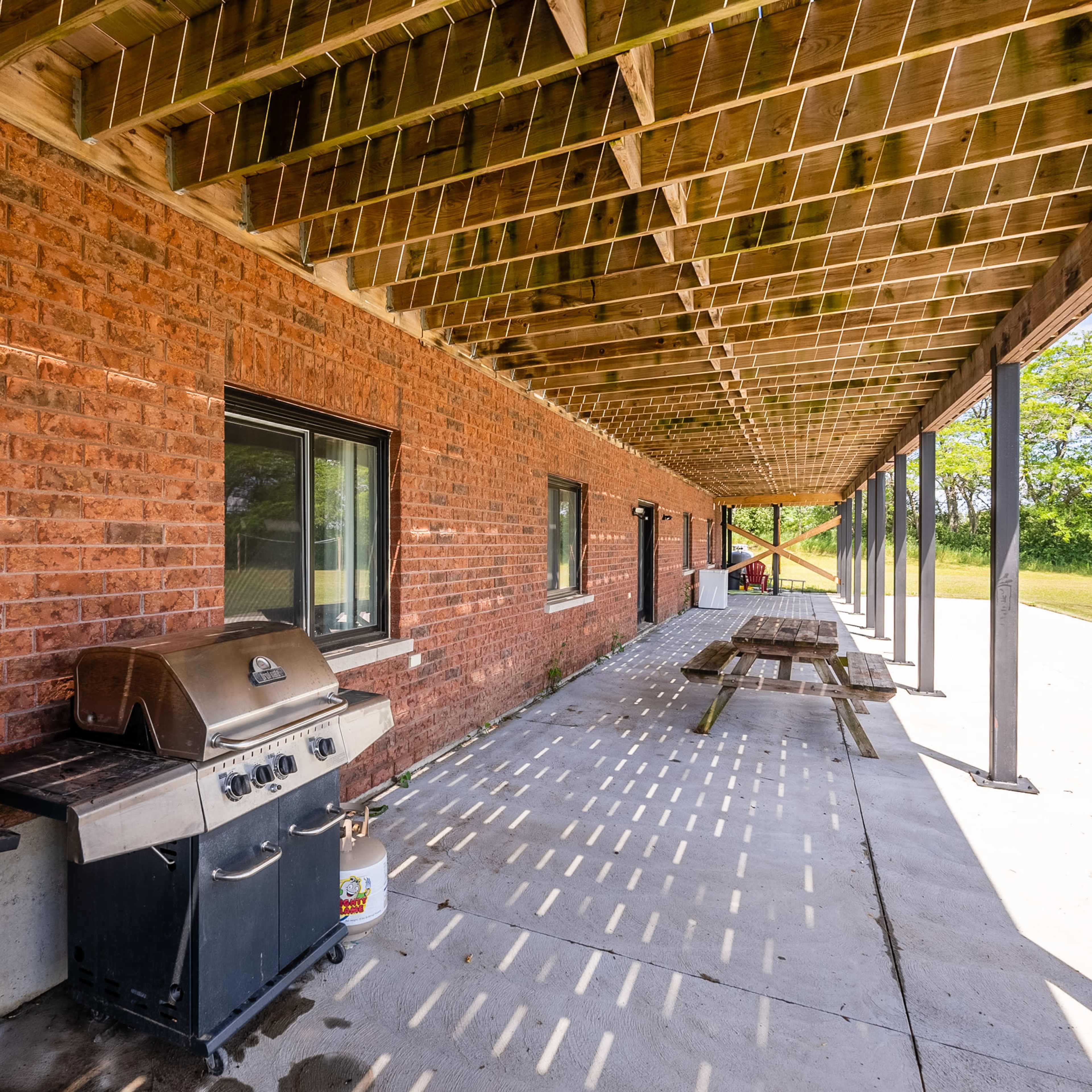 A brick building with a covered porch area that includes two grills and a picnic table.