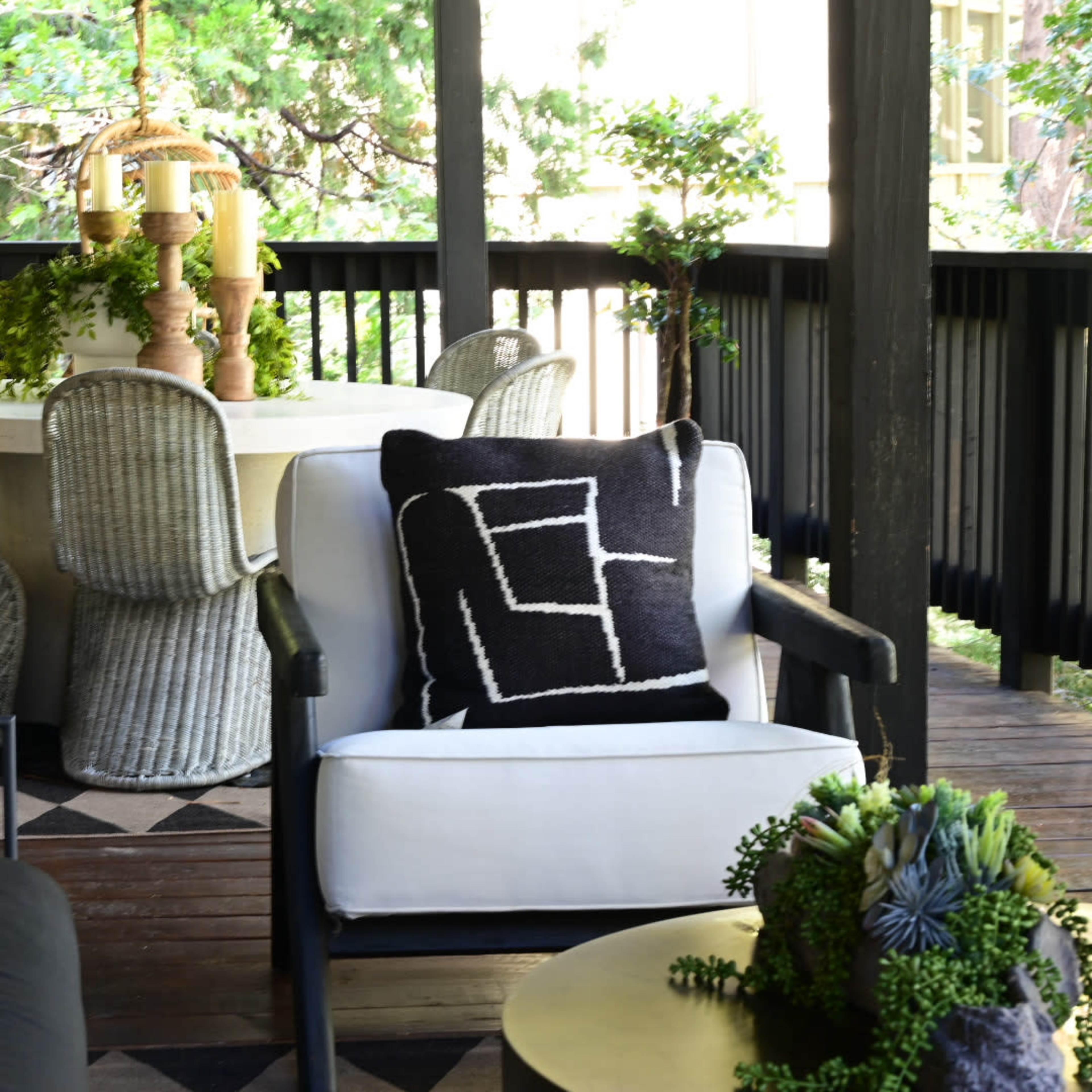 A patio with a round dining table, woven chairs, and a hanging swing, surrounded by greenery.