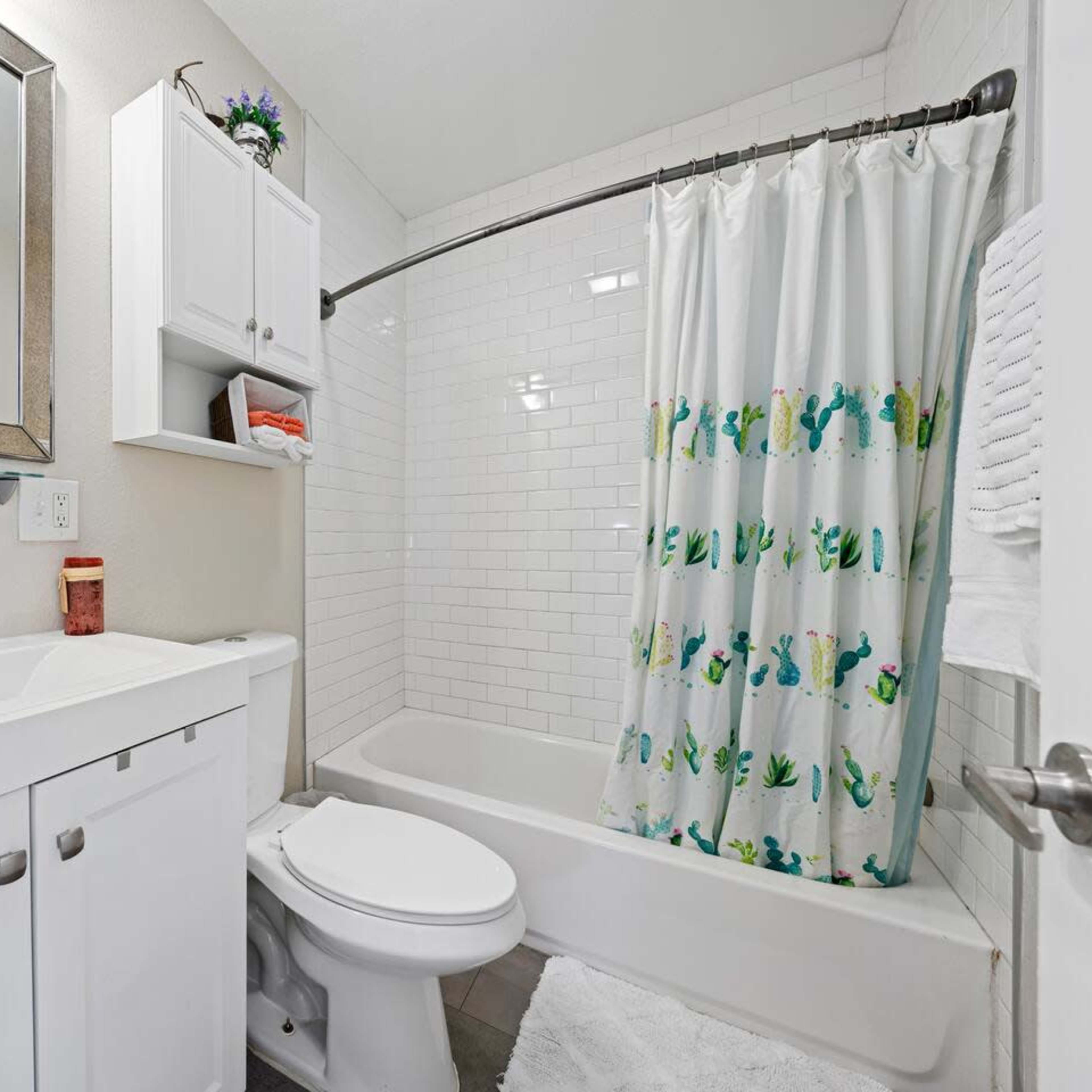 A compact bathroom features a white vanity, a bathtub with a shower curtain, and a mirror above the sink.