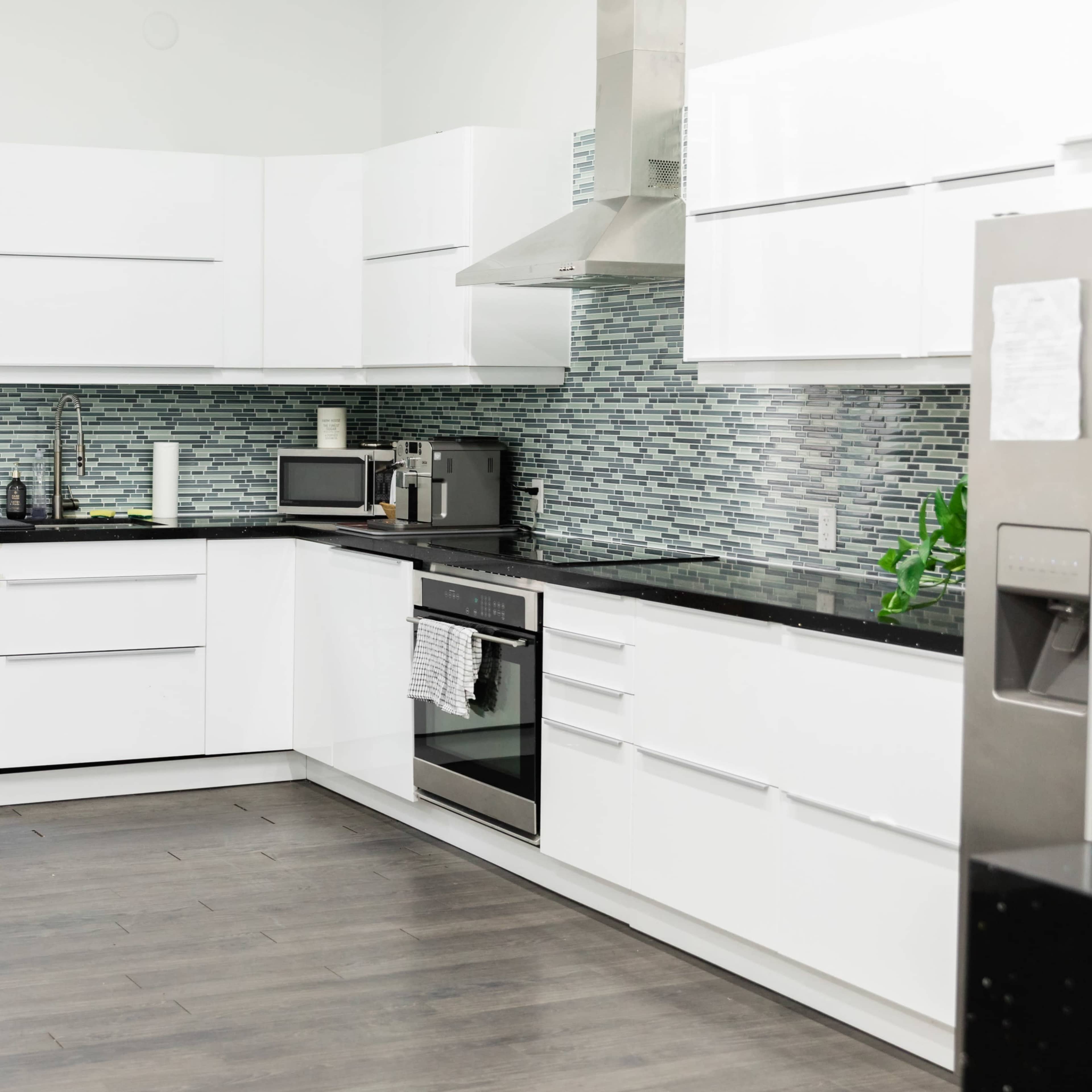 A modern kitchen with white cabinets, a stainless steel refrigerator, and a tiled backsplash.