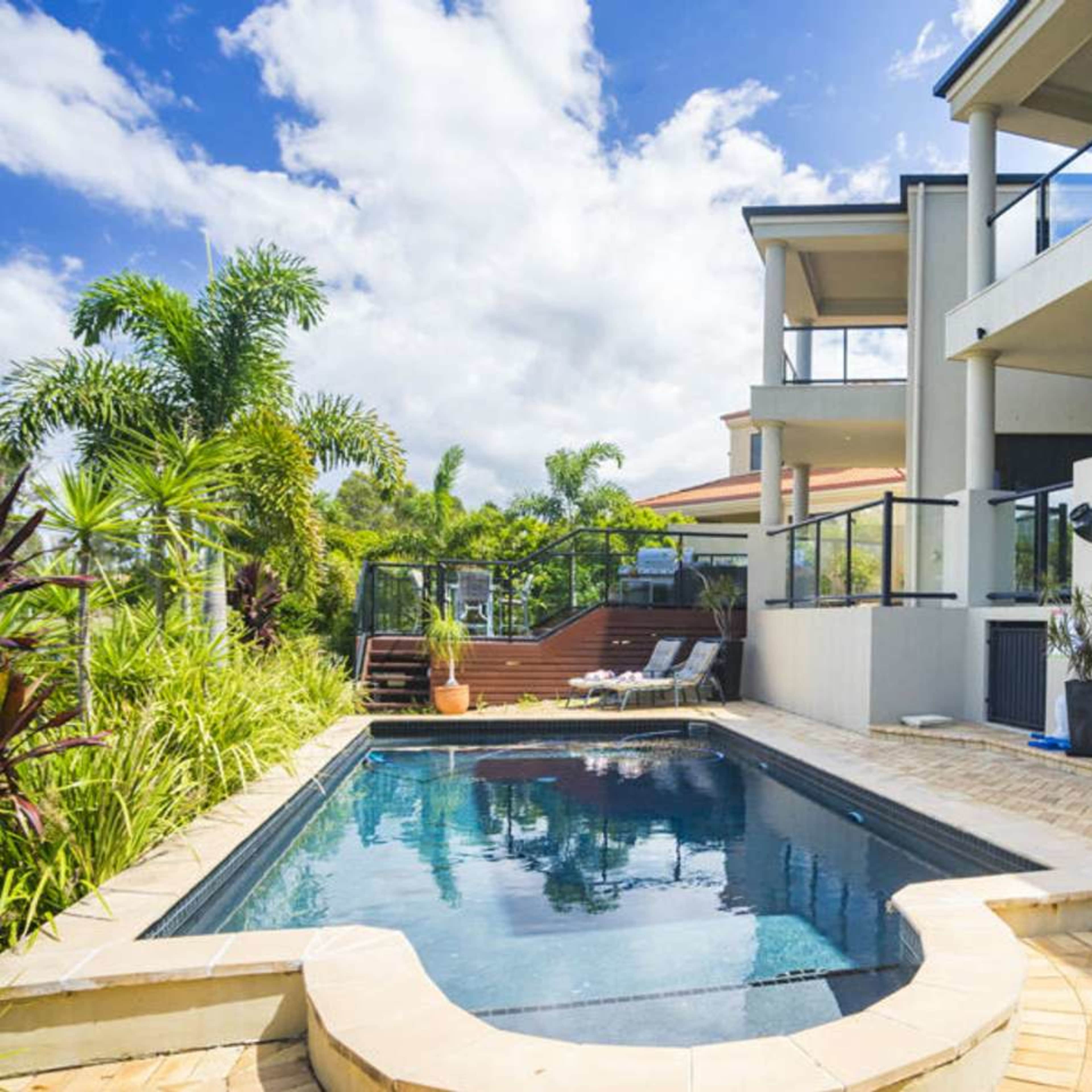 A modern house features a swimming pool surrounded by tropical plants and outdoor seating.