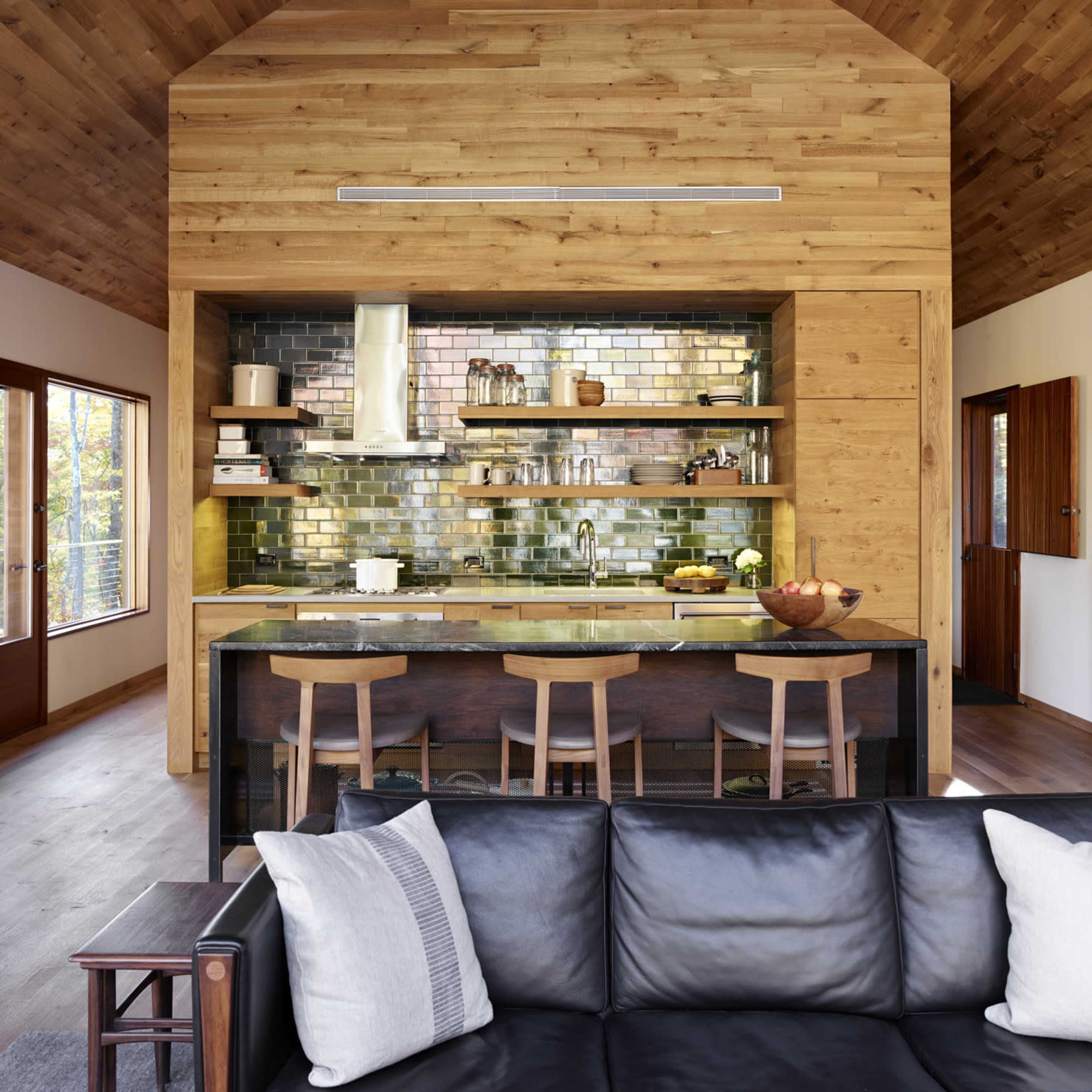A modern kitchen and living area with wooden walls, a large island with bar stools, and large windows allowing light into the space.