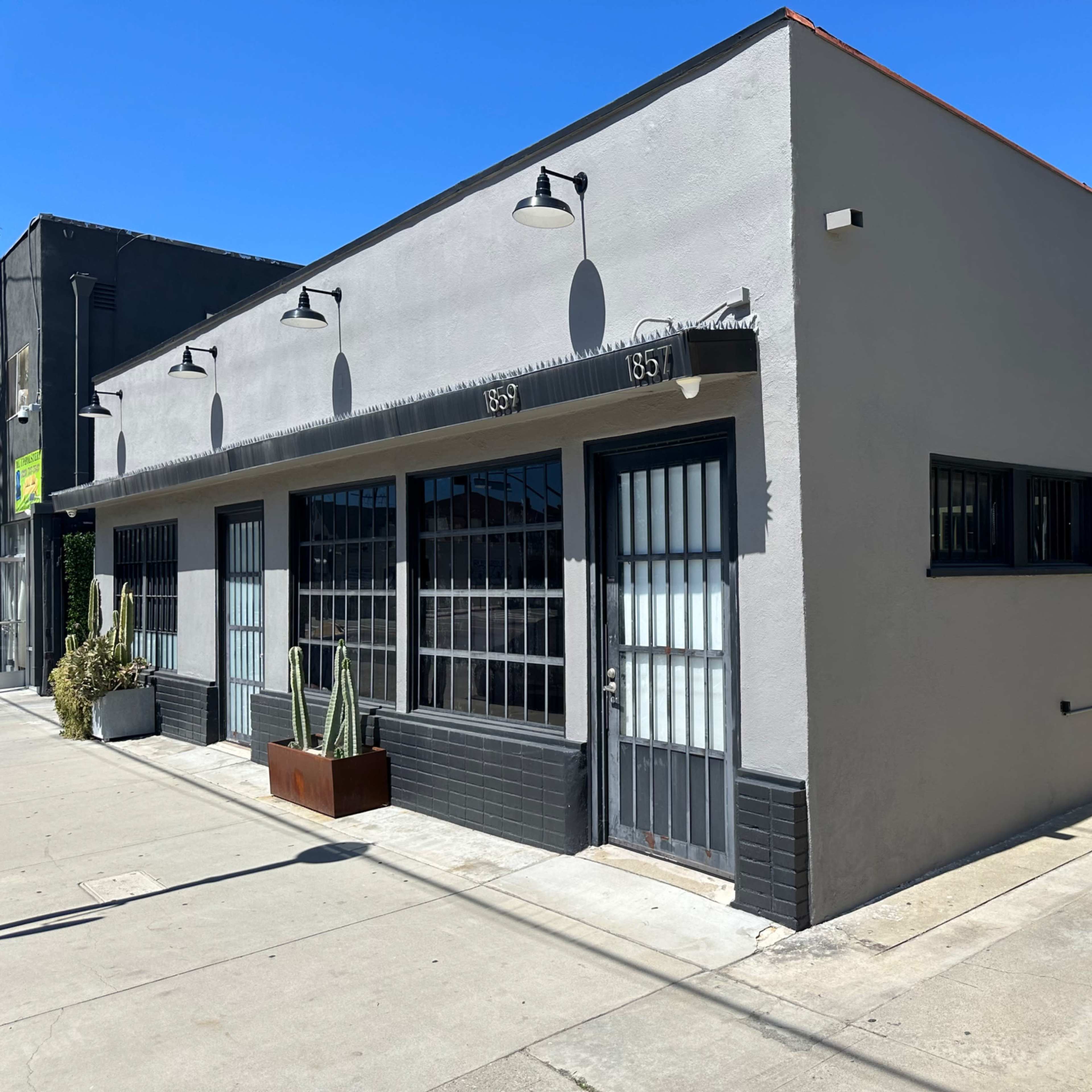 A gray commercial building with large windows and a gated entrance, situated on a sunny street.