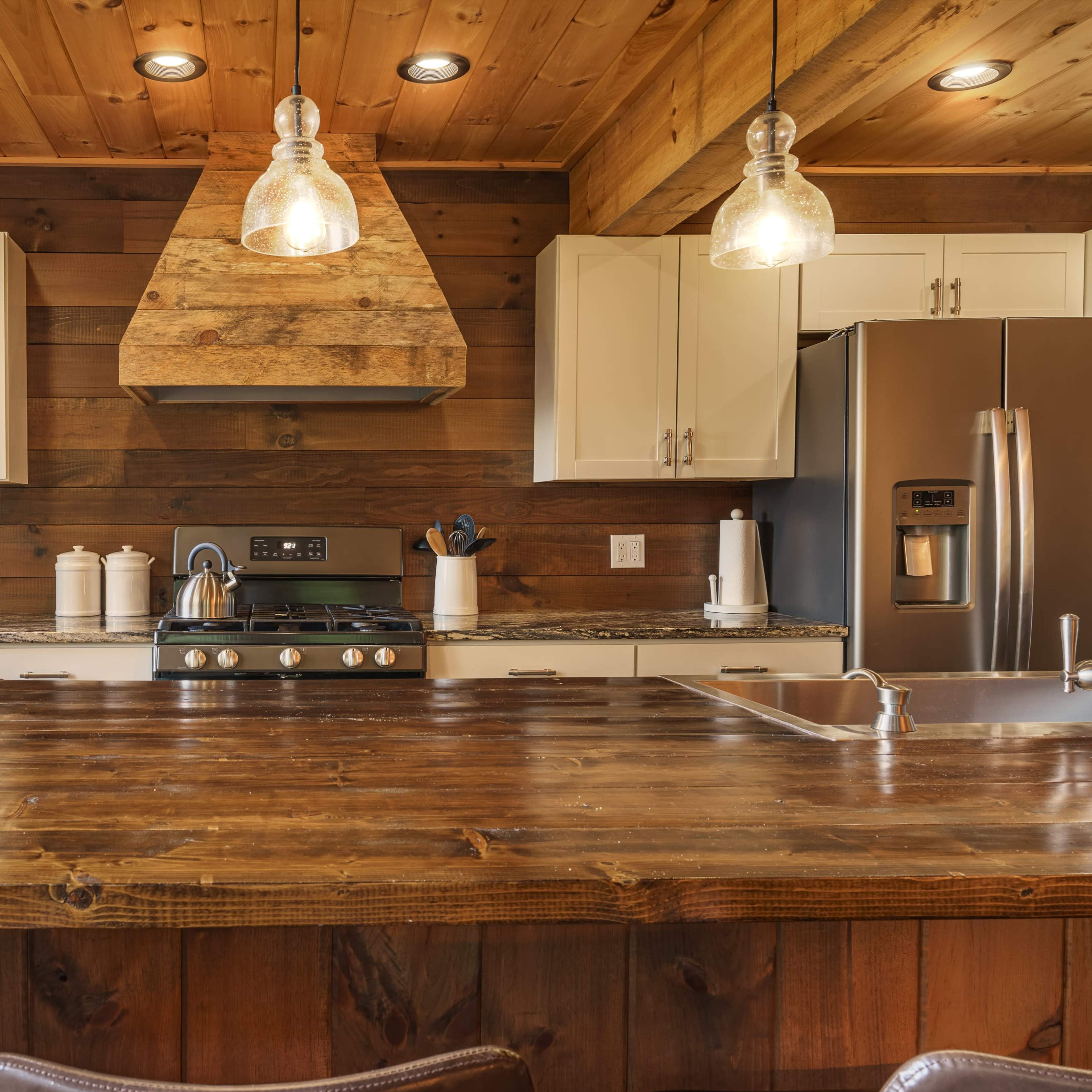 The kitchen features a large wooden island with a gas stove and a stainless steel refrigerator, surrounded by wooden walls and white cabinetry.