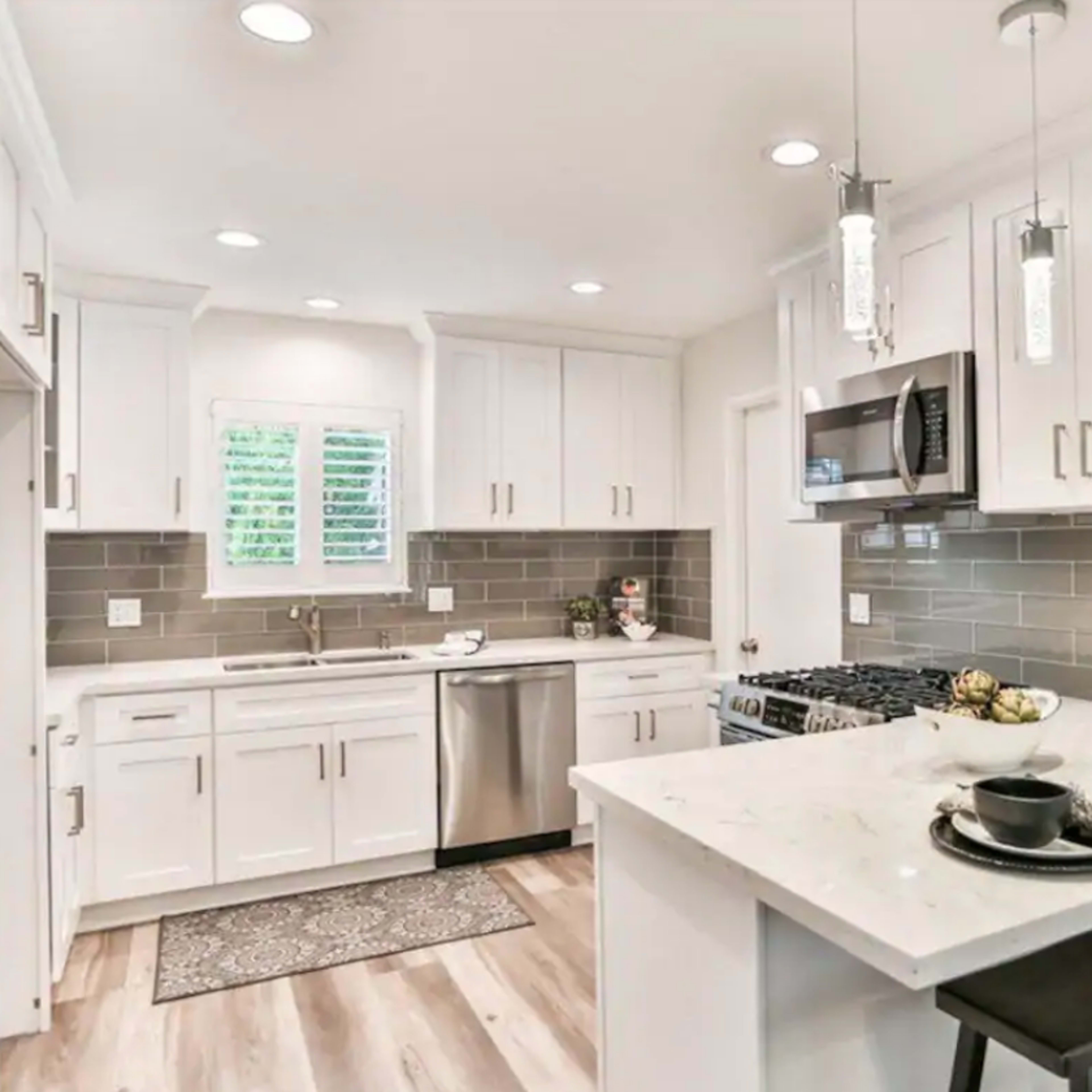 A modern kitchen featuring white cabinetry, stainless steel appliances, and a central island with seating for two.