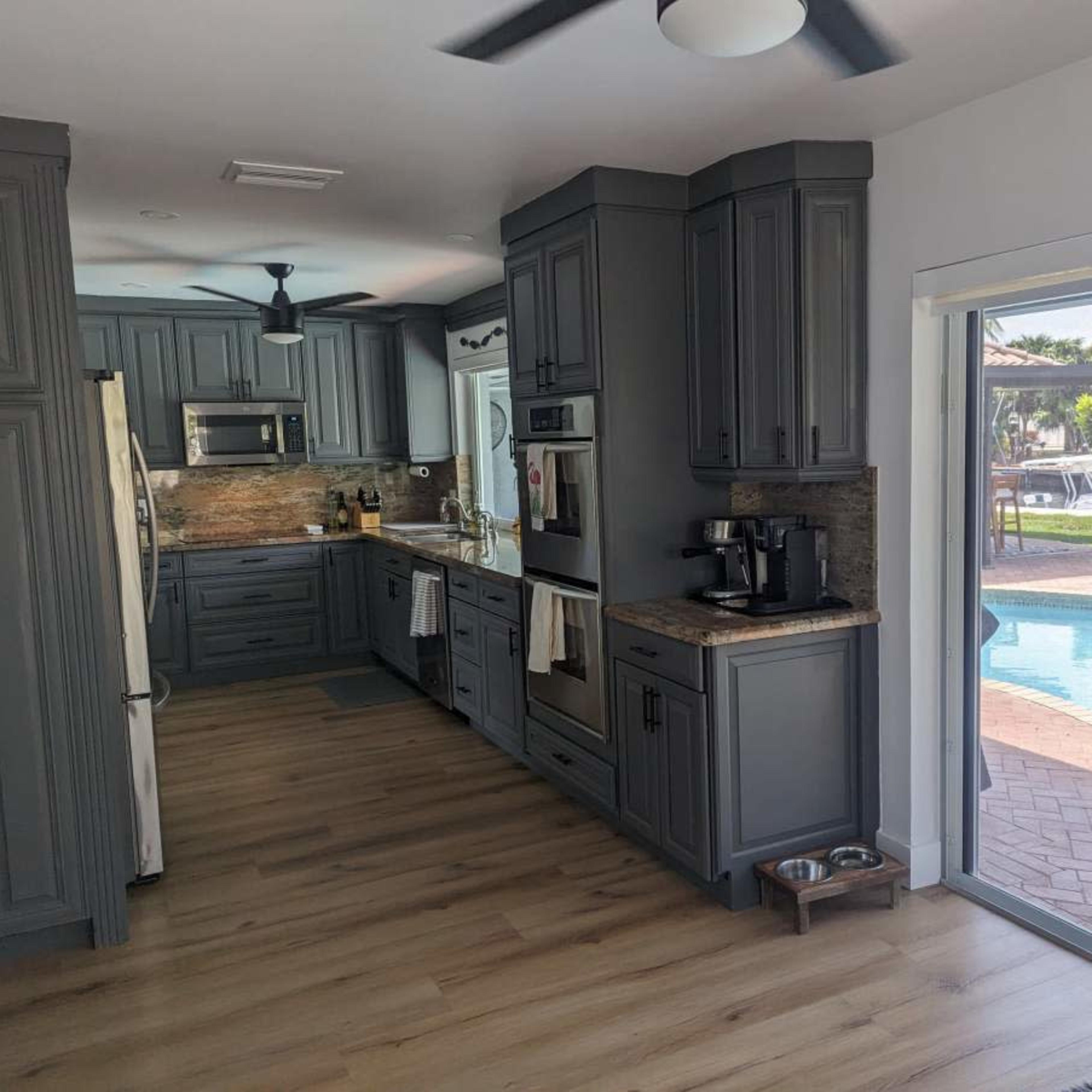 A modern kitchen with gray cabinets, stainless steel appliances, and a view of a pool area through a sliding glass door.