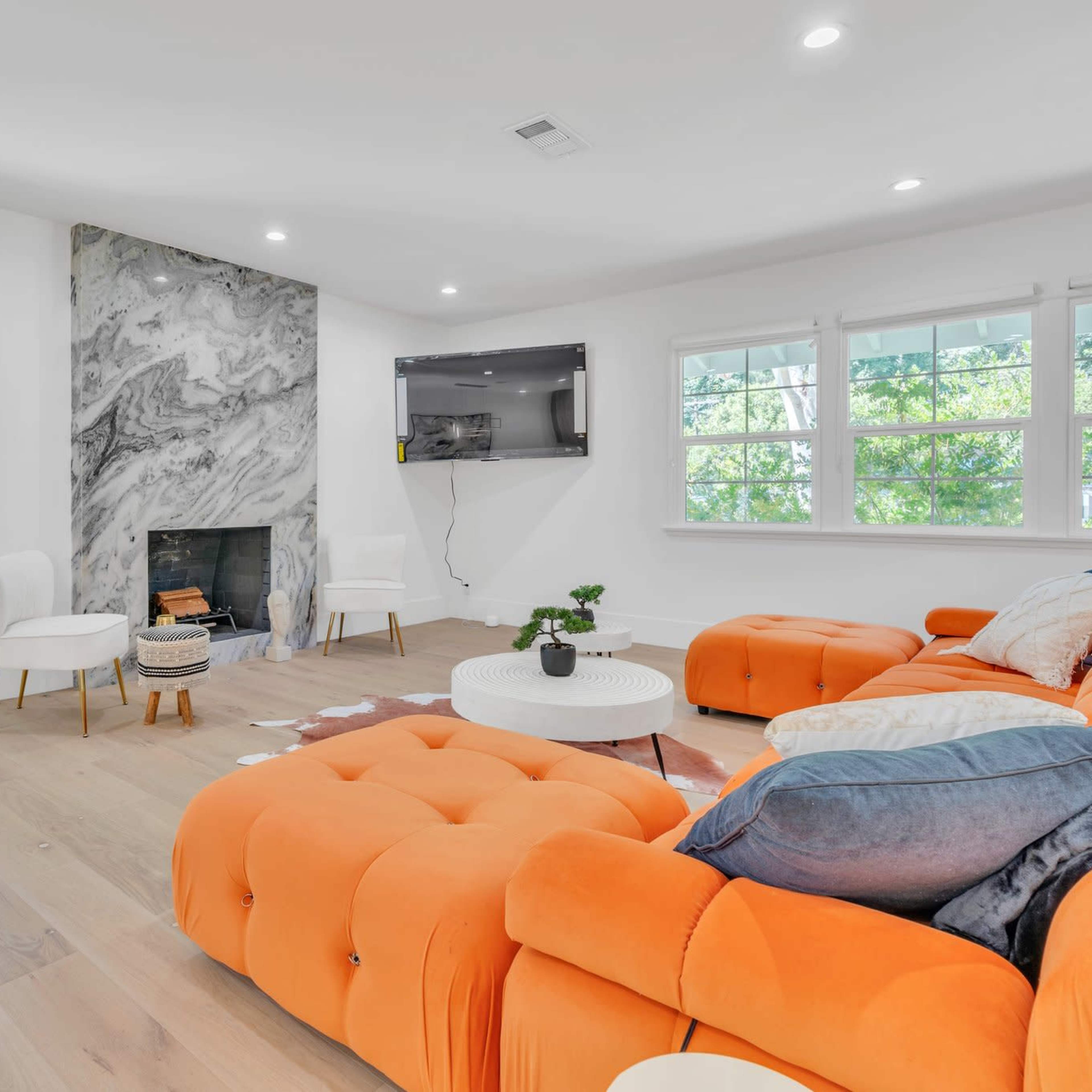 The living room features an orange sectional sofa, a white coffee table, and a marble accent wall with a fireplace.