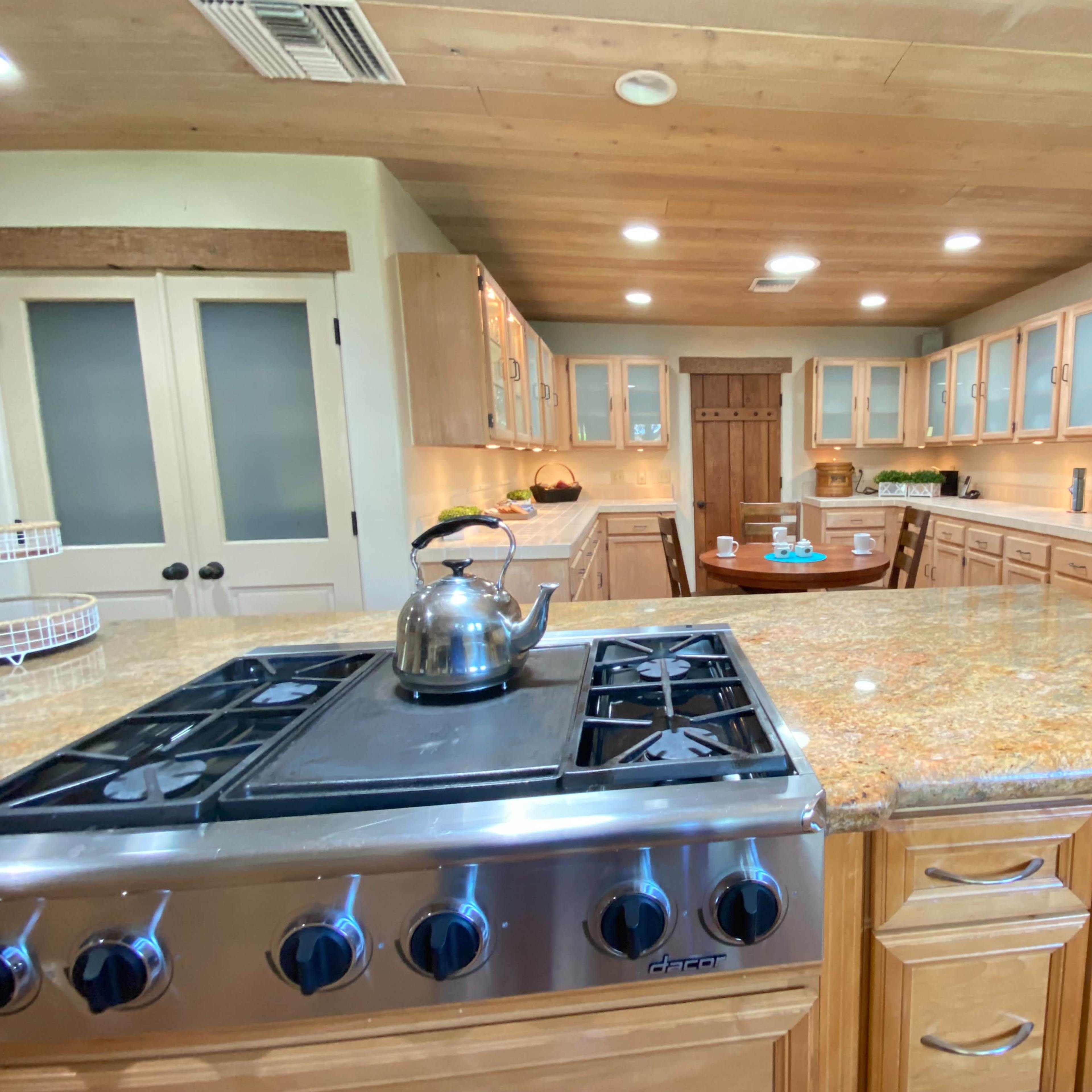 A spacious kitchen featuring wooden cabinets, a granite countertop, and a stove with a kettle on it.