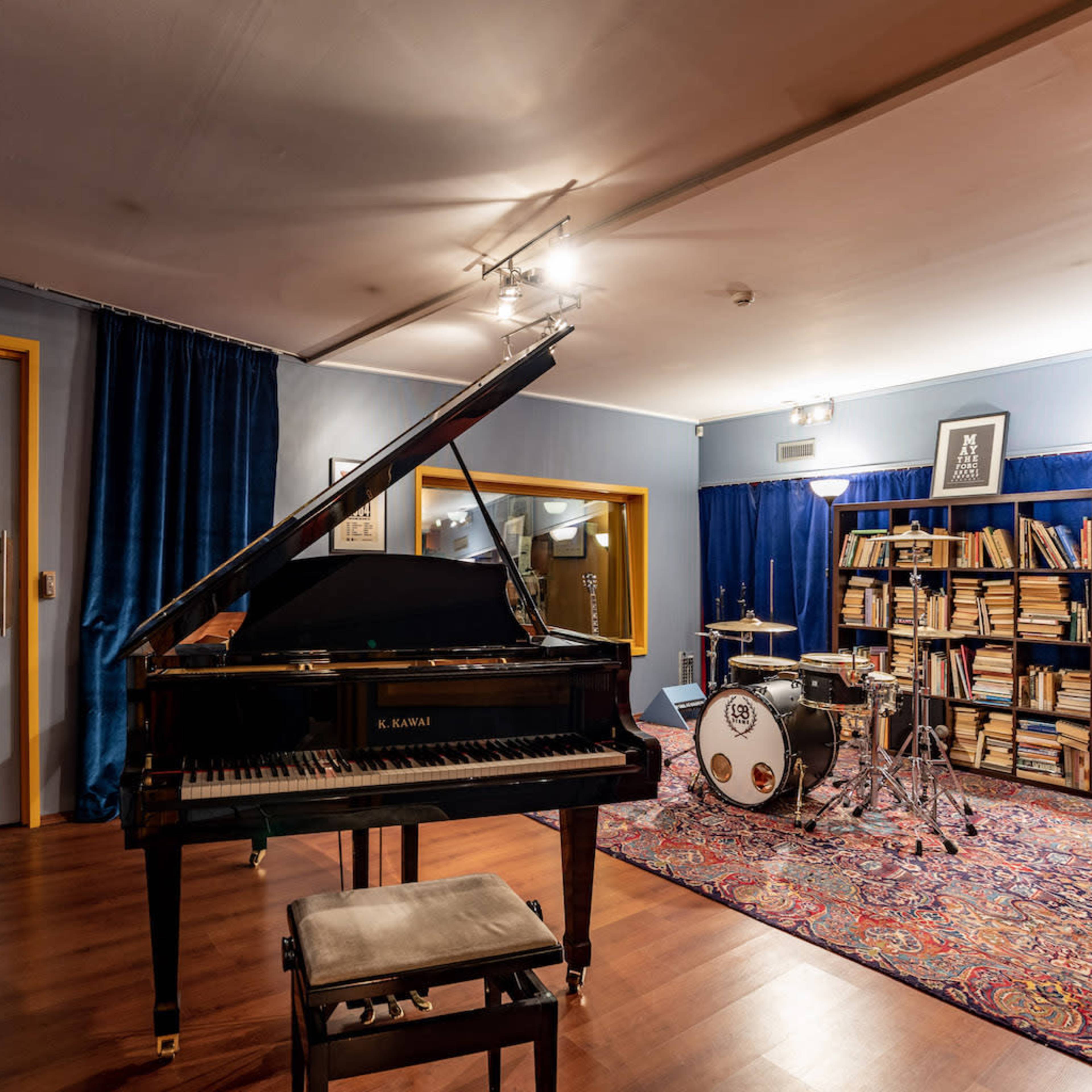 A music studio featuring a grand piano, a drum set, and shelves filled with books.
