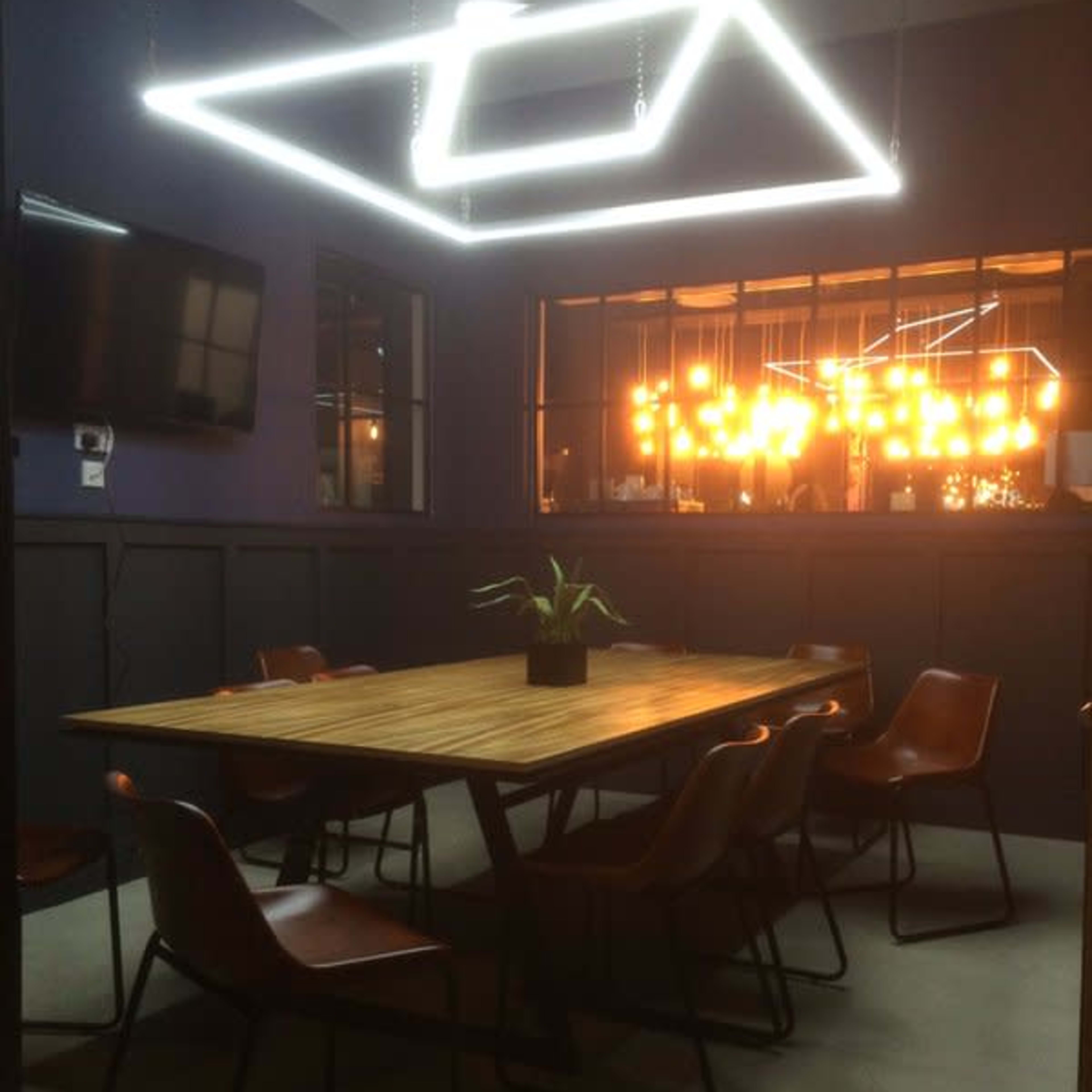 A well-lit dining area features a wooden table surrounded by eight chairs, with a dramatic overhead light fixture illuminating the space.