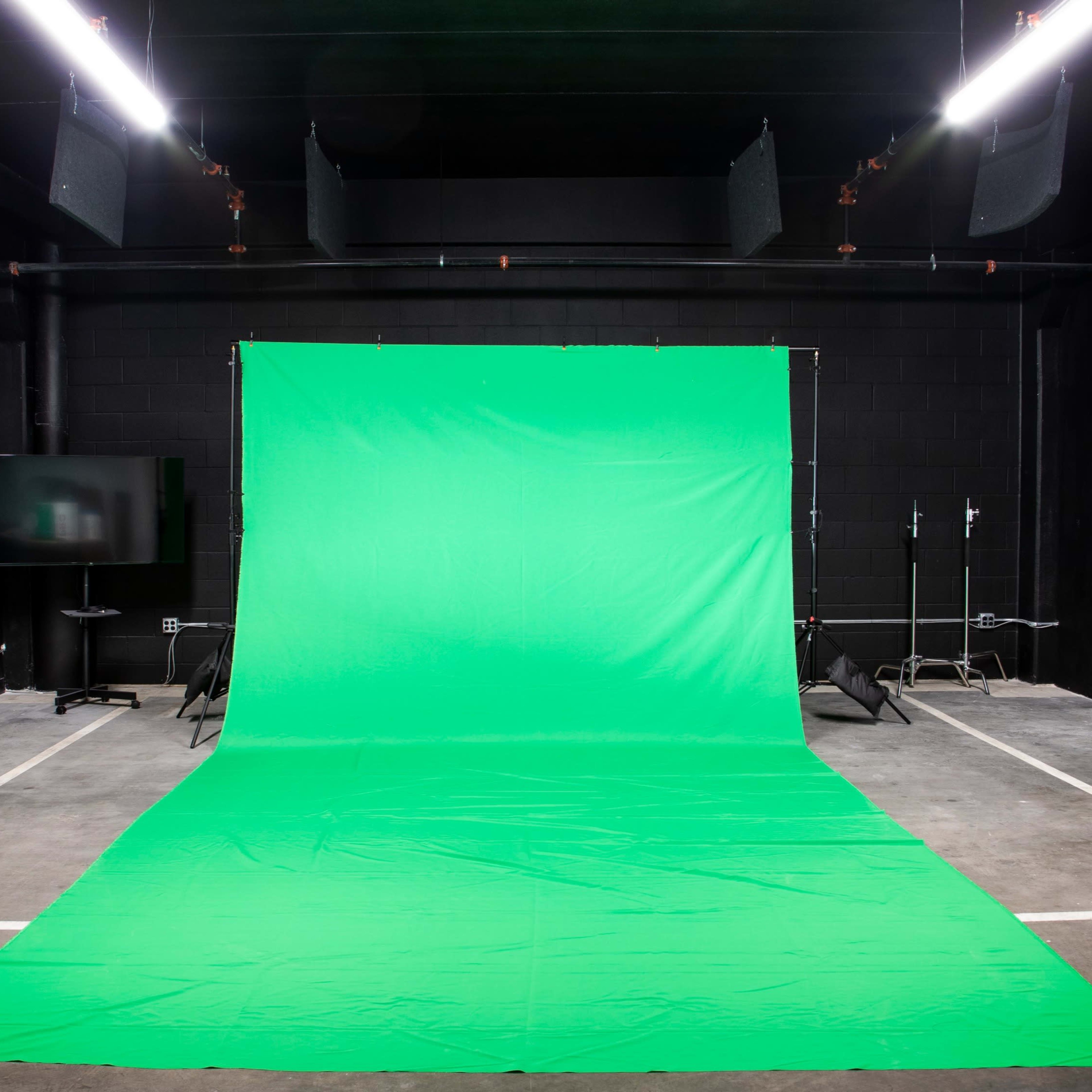 An empty studio space featuring a green backdrop, floor, and minimal equipment in a dimly lit environment.
