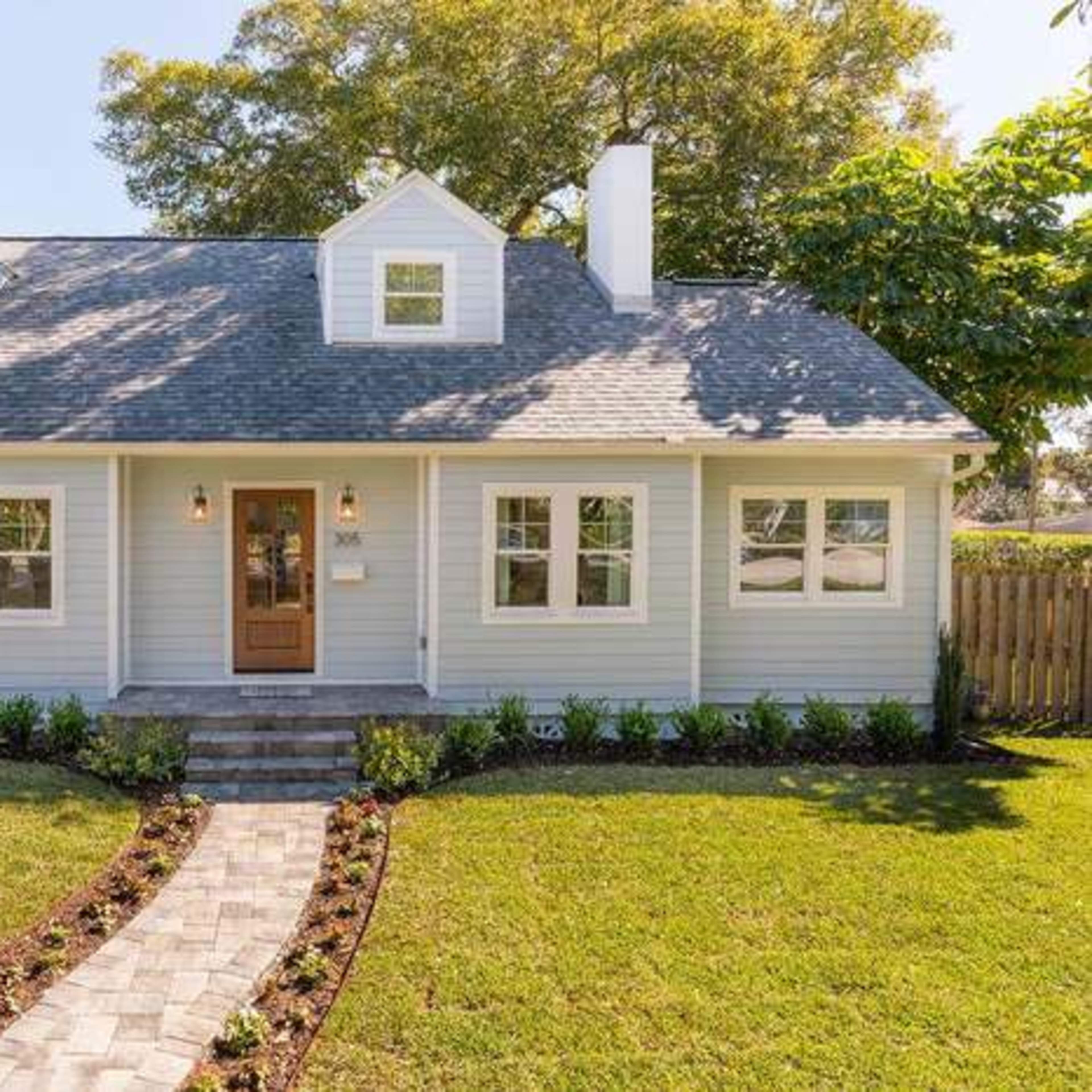 A light blue, one-and-a-half-story house with a front porch and a landscaped garden path leading up to the entrance.