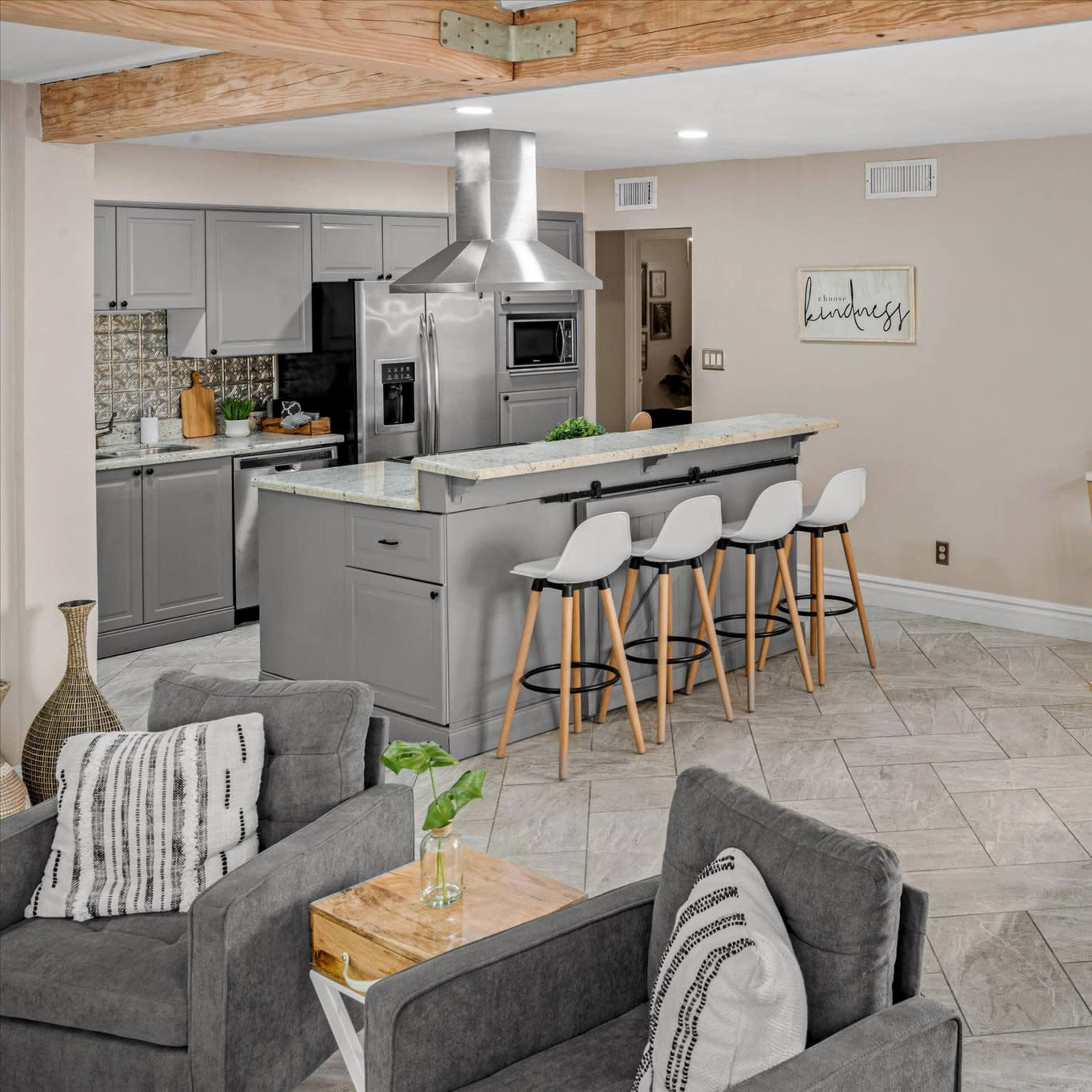 A modern open-concept kitchen and dining area featuring gray cabinets, a large island with seating, and a wooden dining table set for four.