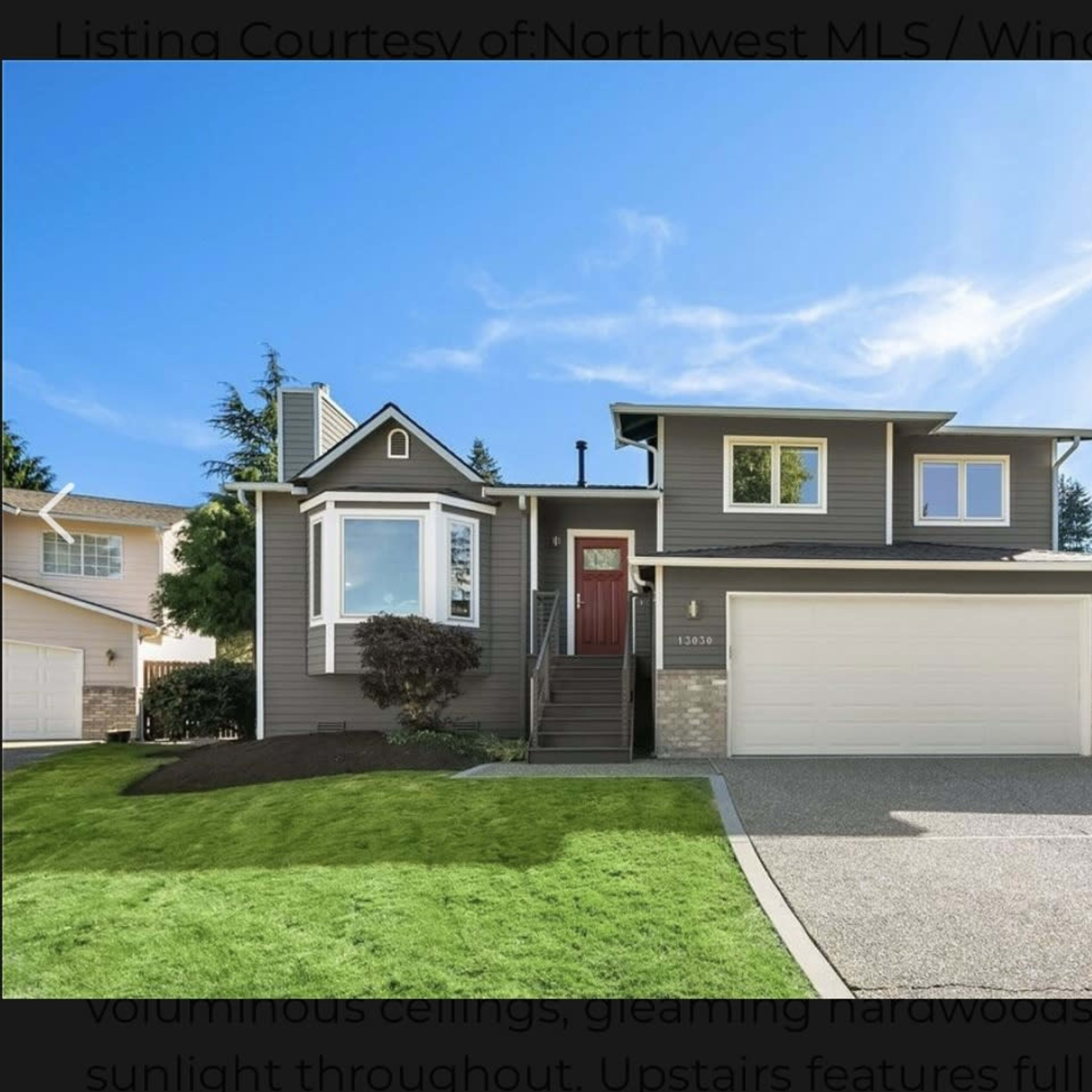 A modern two-story house with a dark exterior, large windows, and a neatly landscaped front yard.