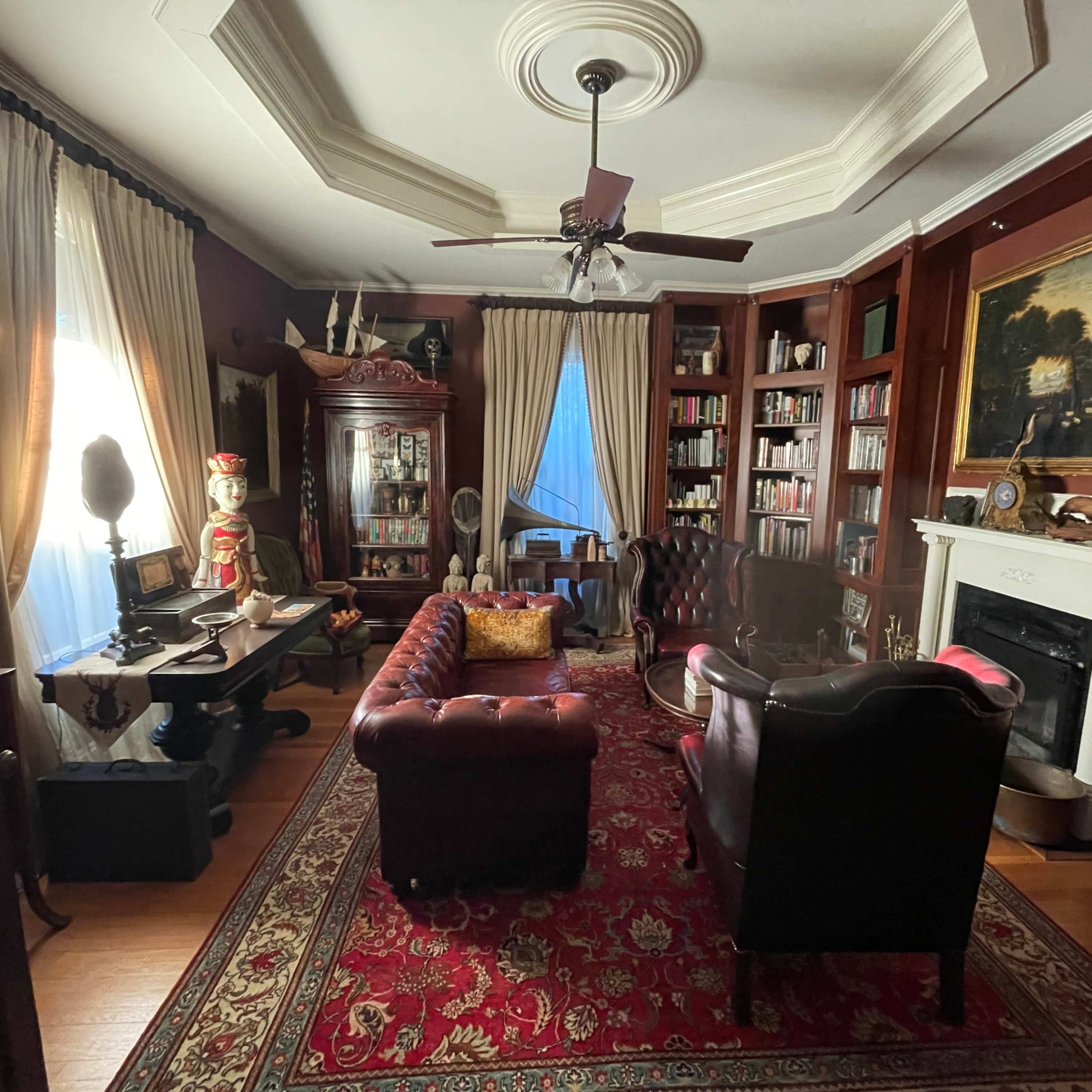 A vintage-style living room with dark wood bookshelves, a leather sofa, and a large ornate painting above a fireplace.