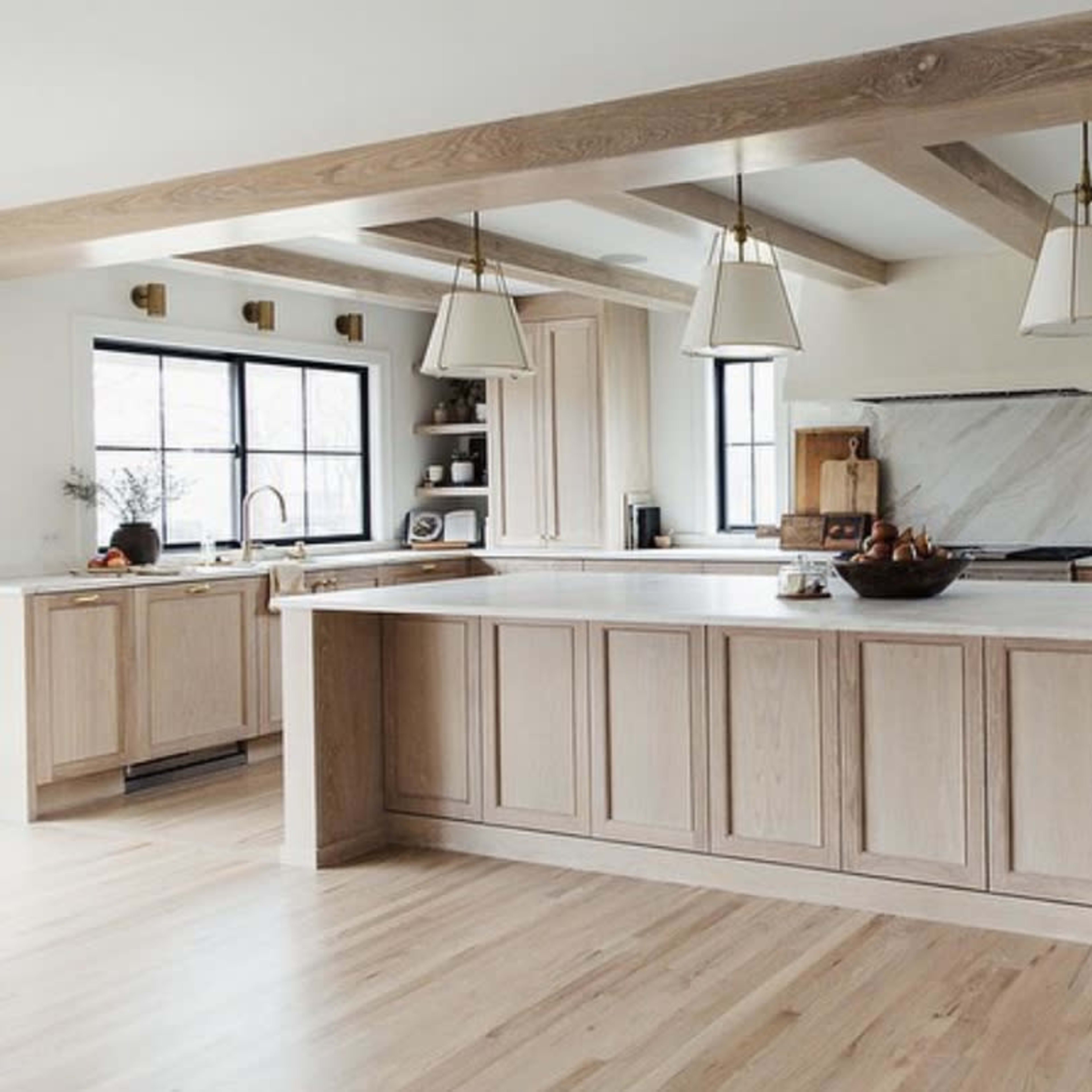 The kitchen features light wood cabinetry, a large island with a marble countertop, and pendant lighting.