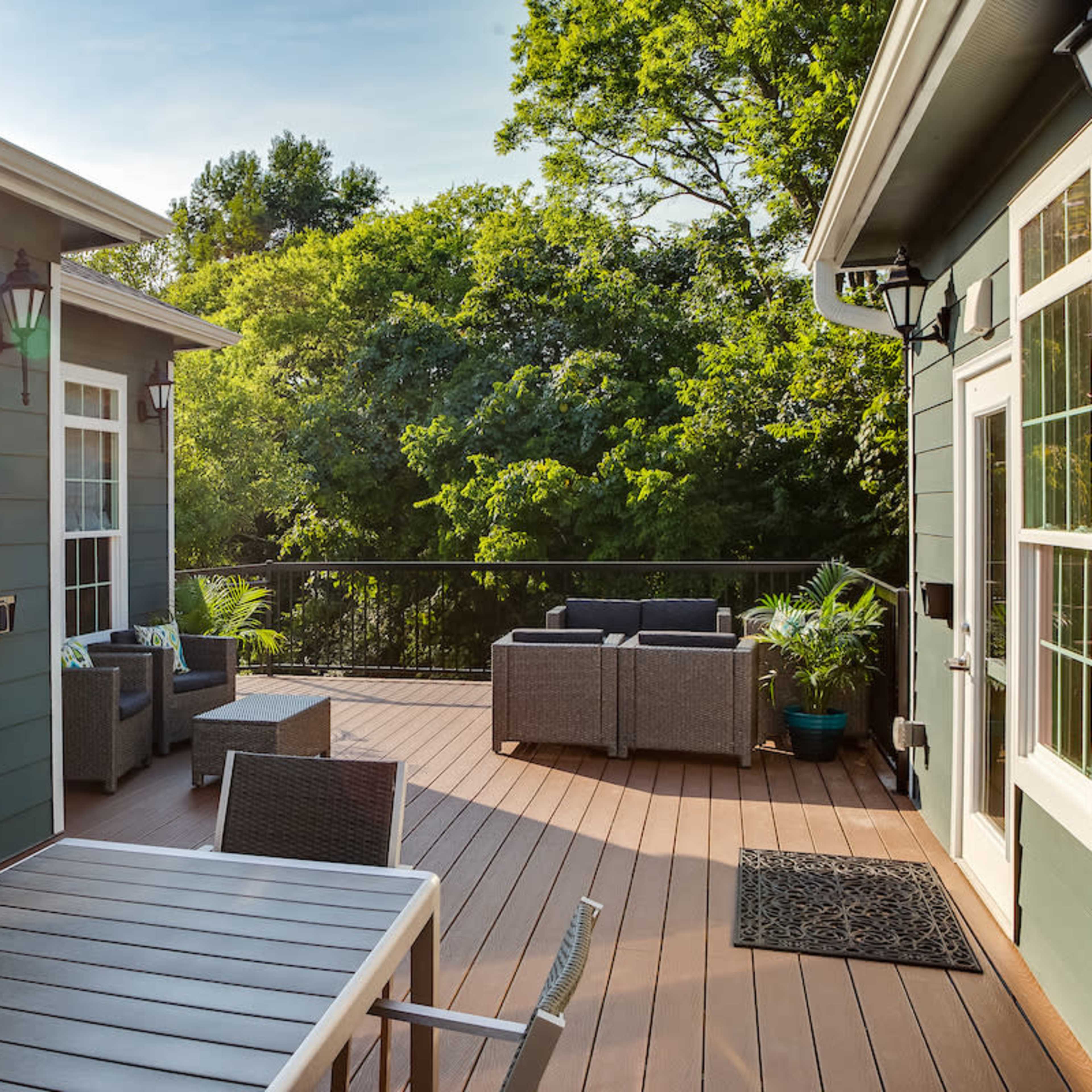 A deck area features modern outdoor furniture and is surrounded by lush greenery.