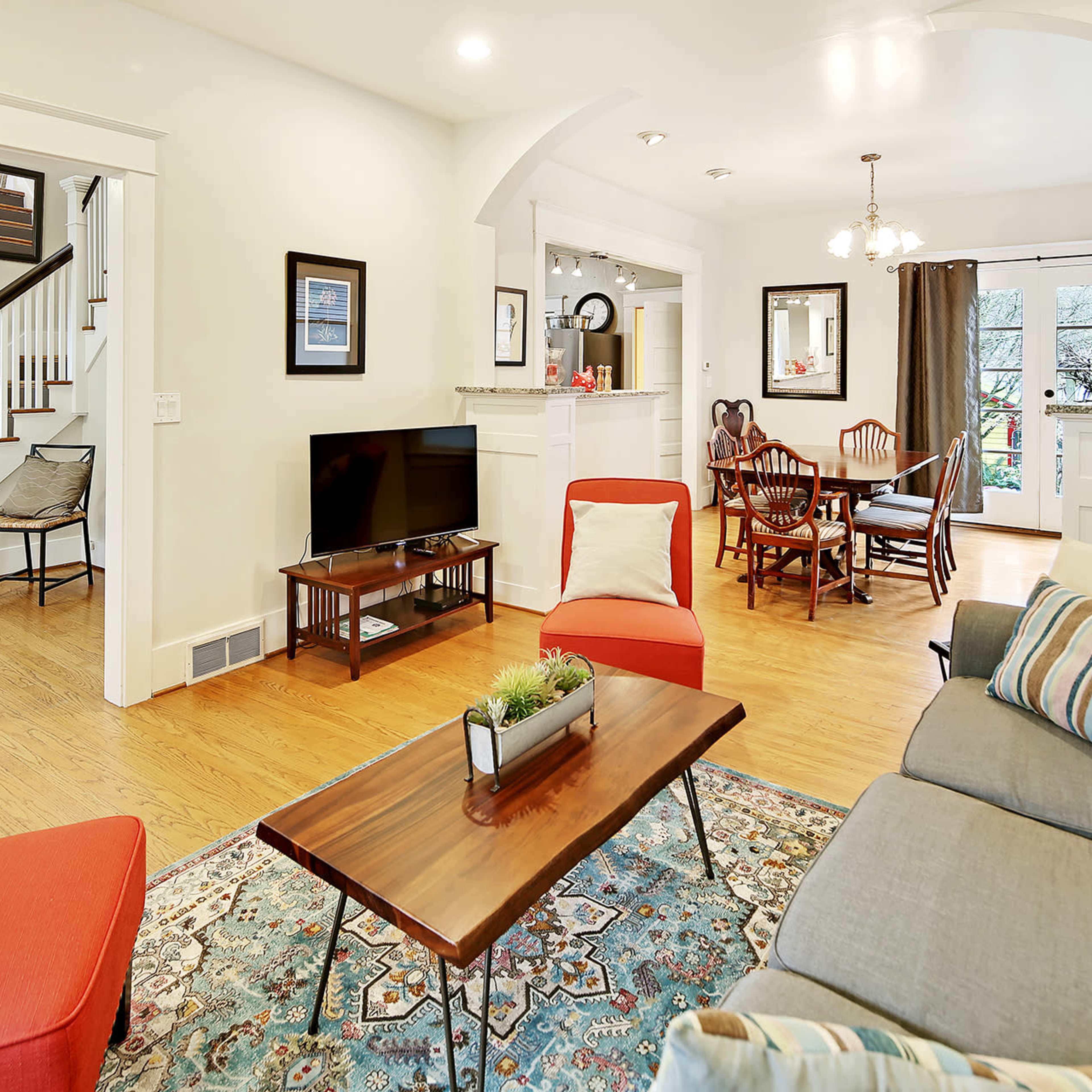 A living room with a gray sofa, red accent chairs, a coffee table, and a connected dining area featuring a round table with chairs and large windows.