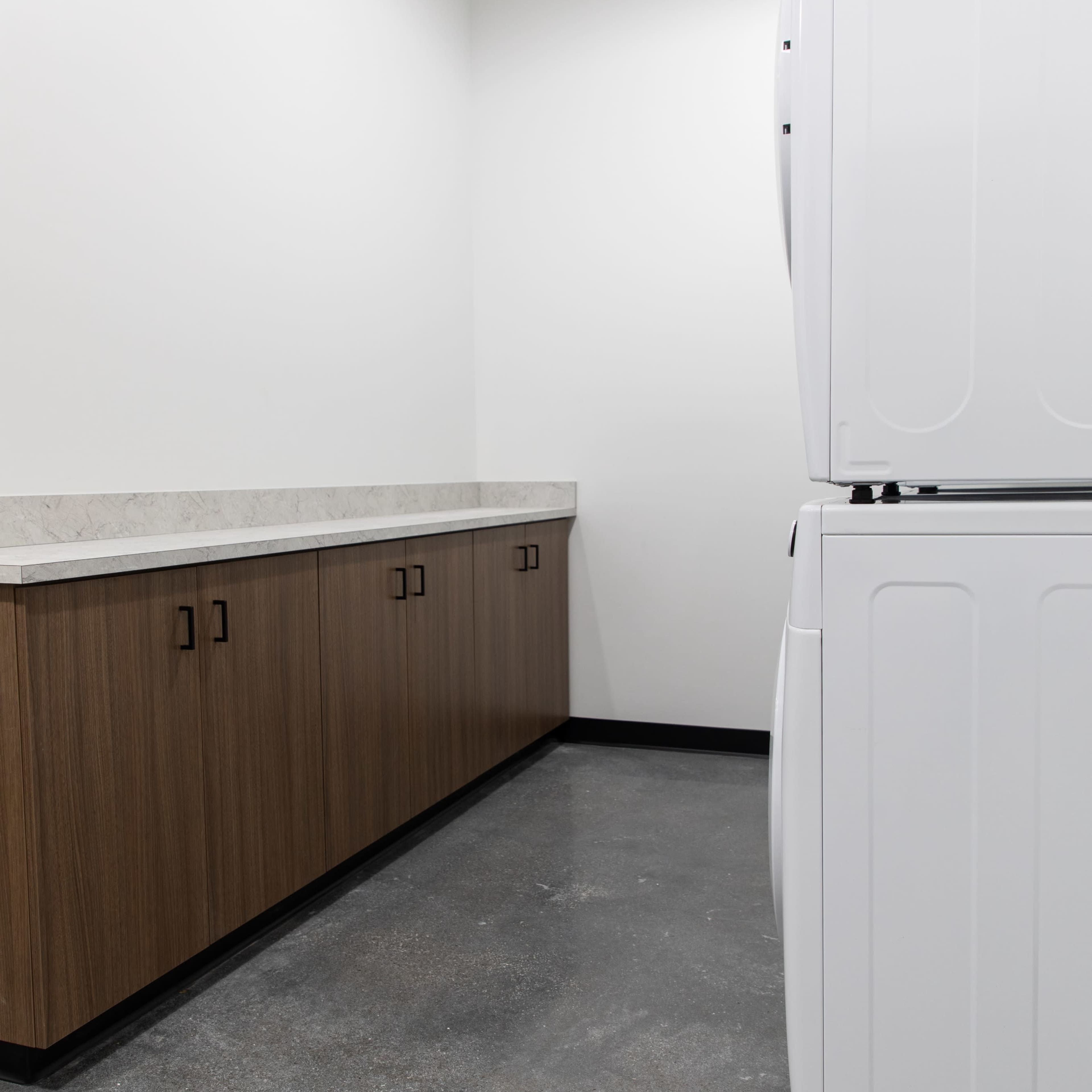 A corner of a laundry room featuring a stacked washer and dryer beside a wooden cabinet and a countertop.