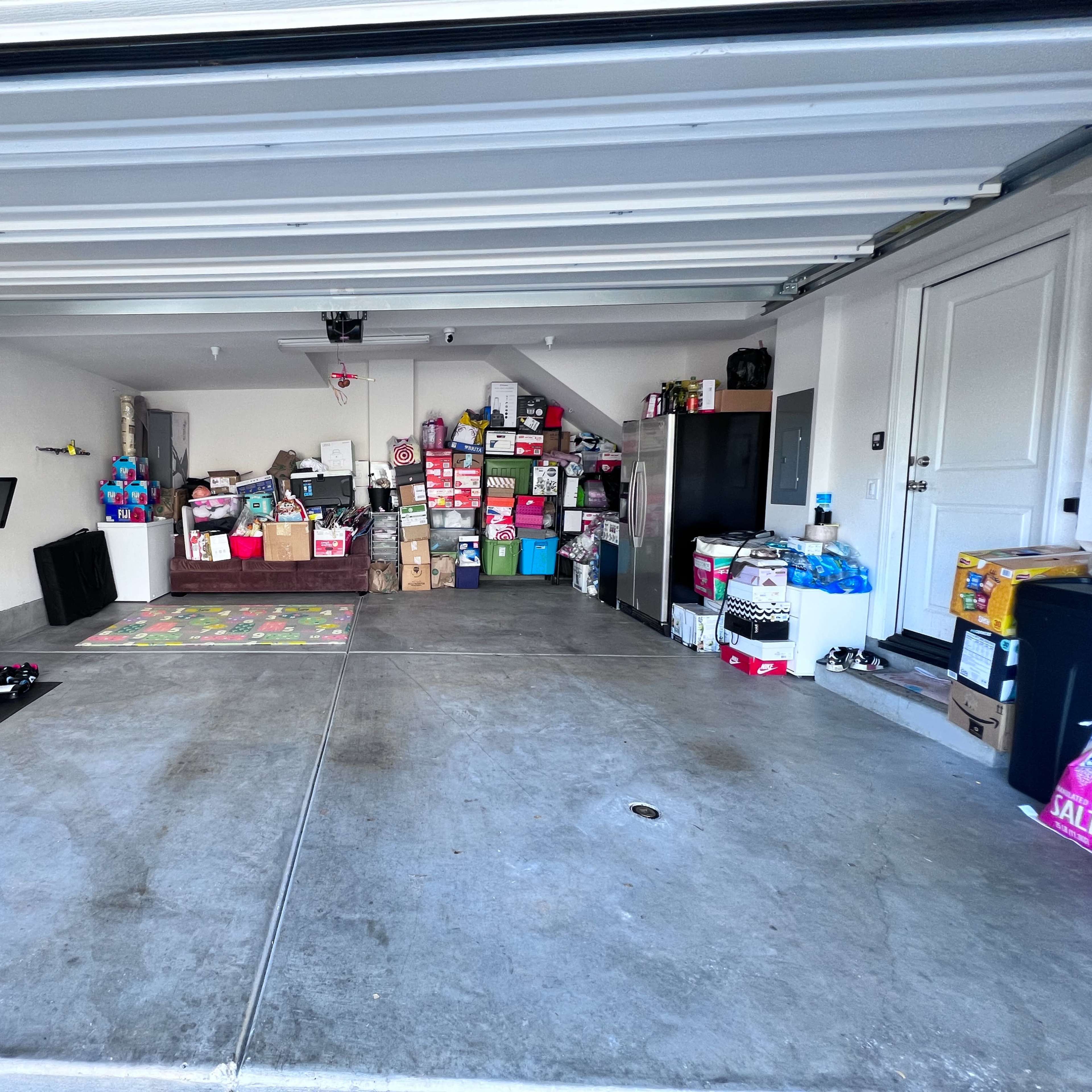 A garage with a mix of stacked boxes, a stationary bike, and shelves filled with various items.