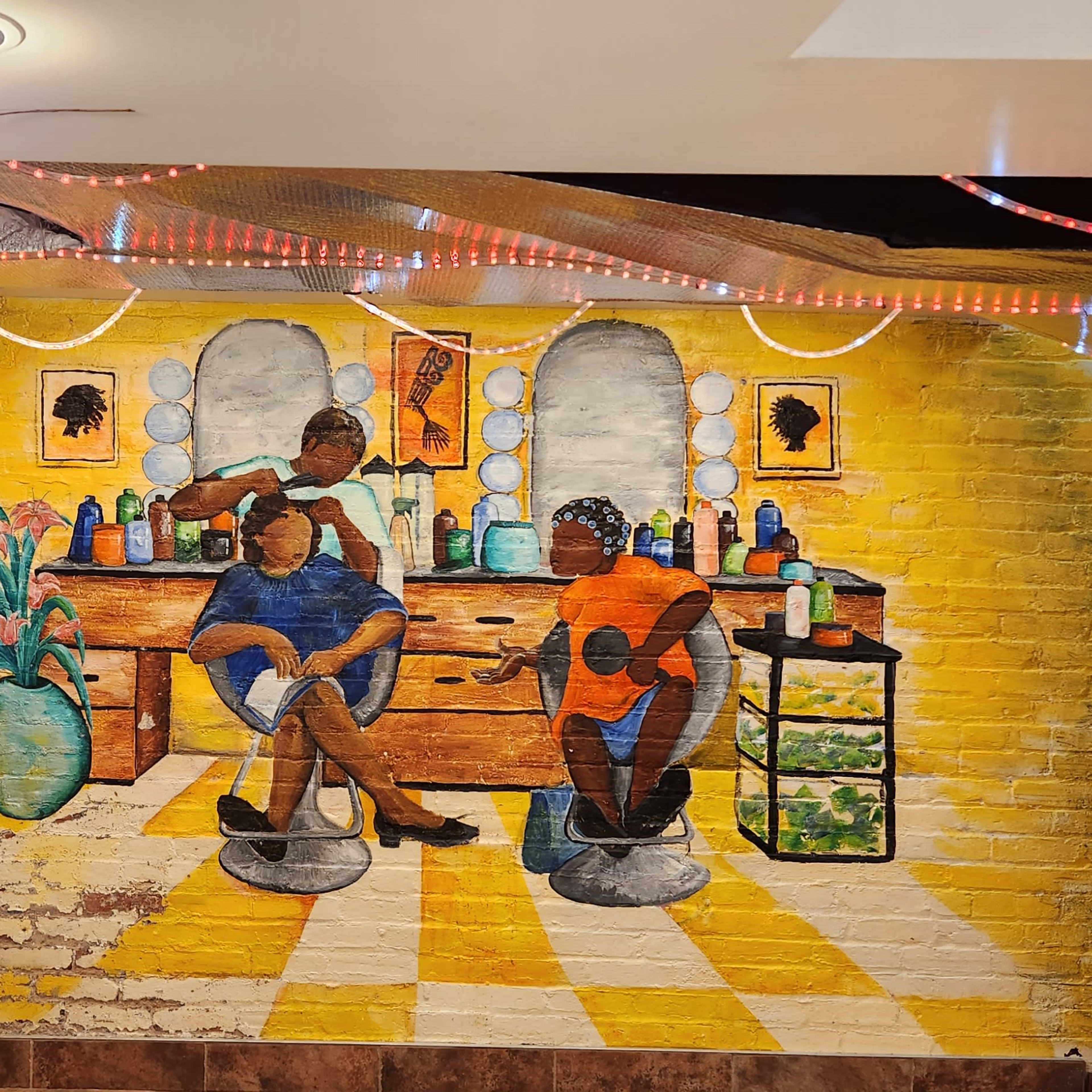 The mural depicts two individuals sitting in salon chairs, surrounded by beauty products and a vibrant interior.
