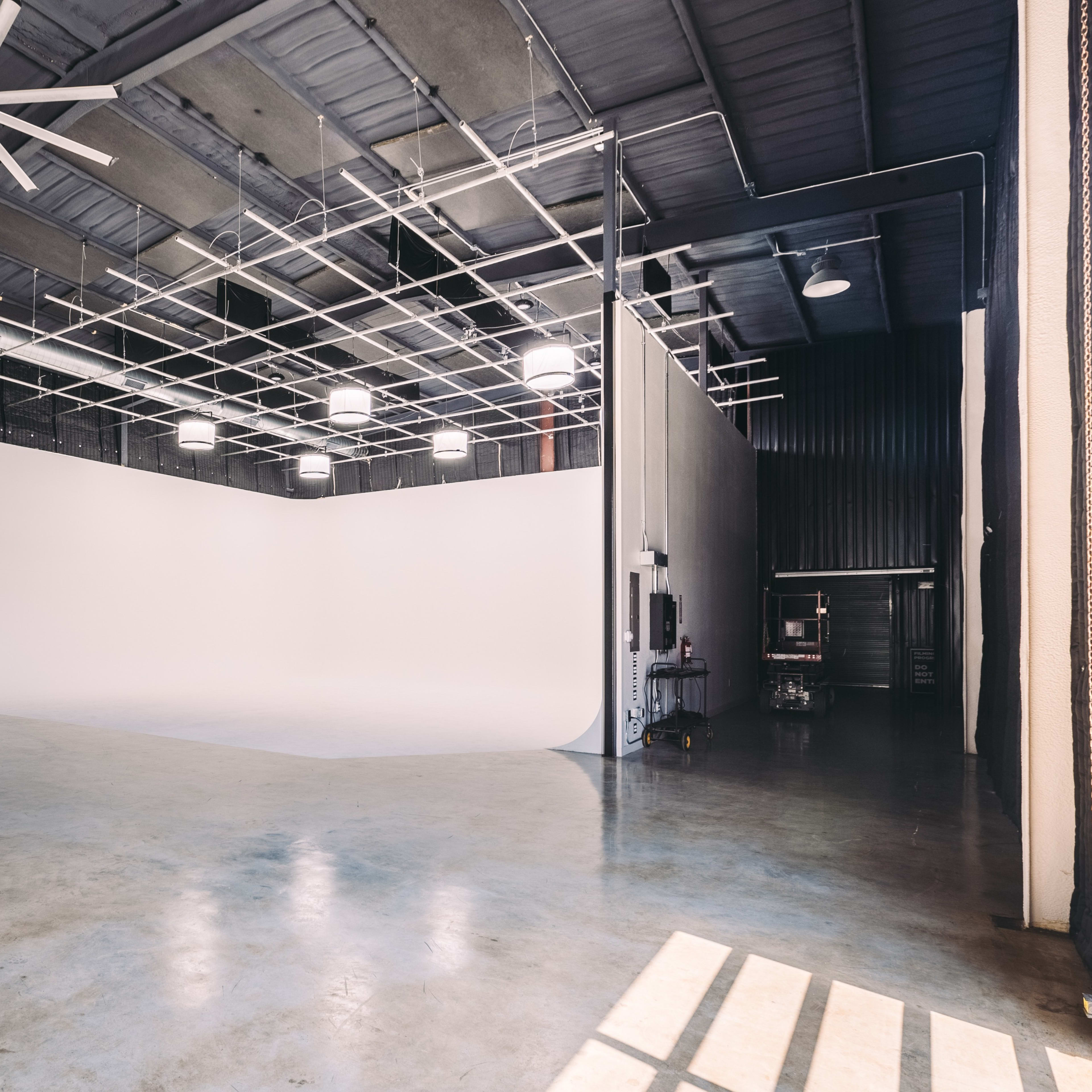 An empty photo studio with a large, white seamless backdrop and high ceilings.