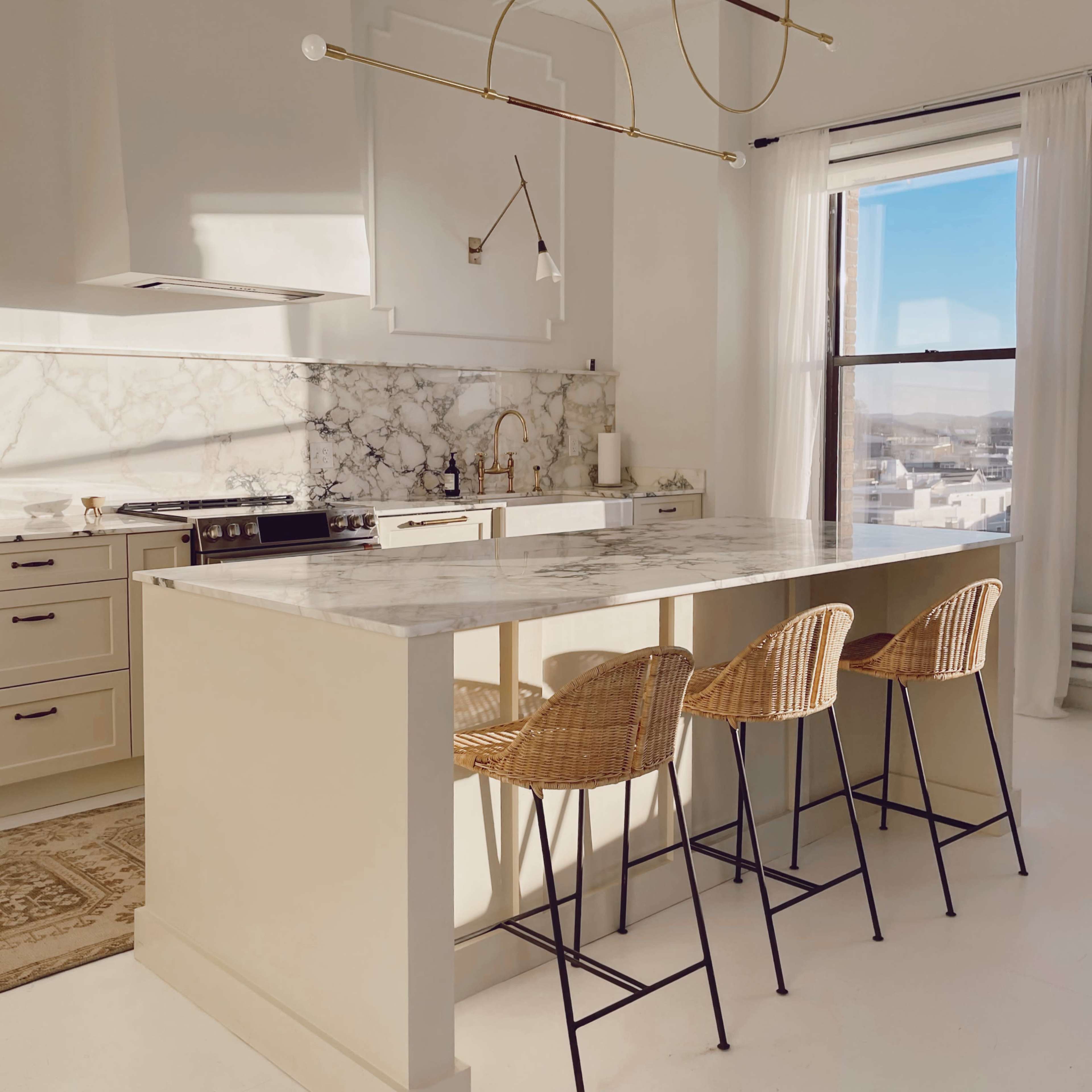 A modern kitchen with a marble countertop island and four wicker bar stools.
