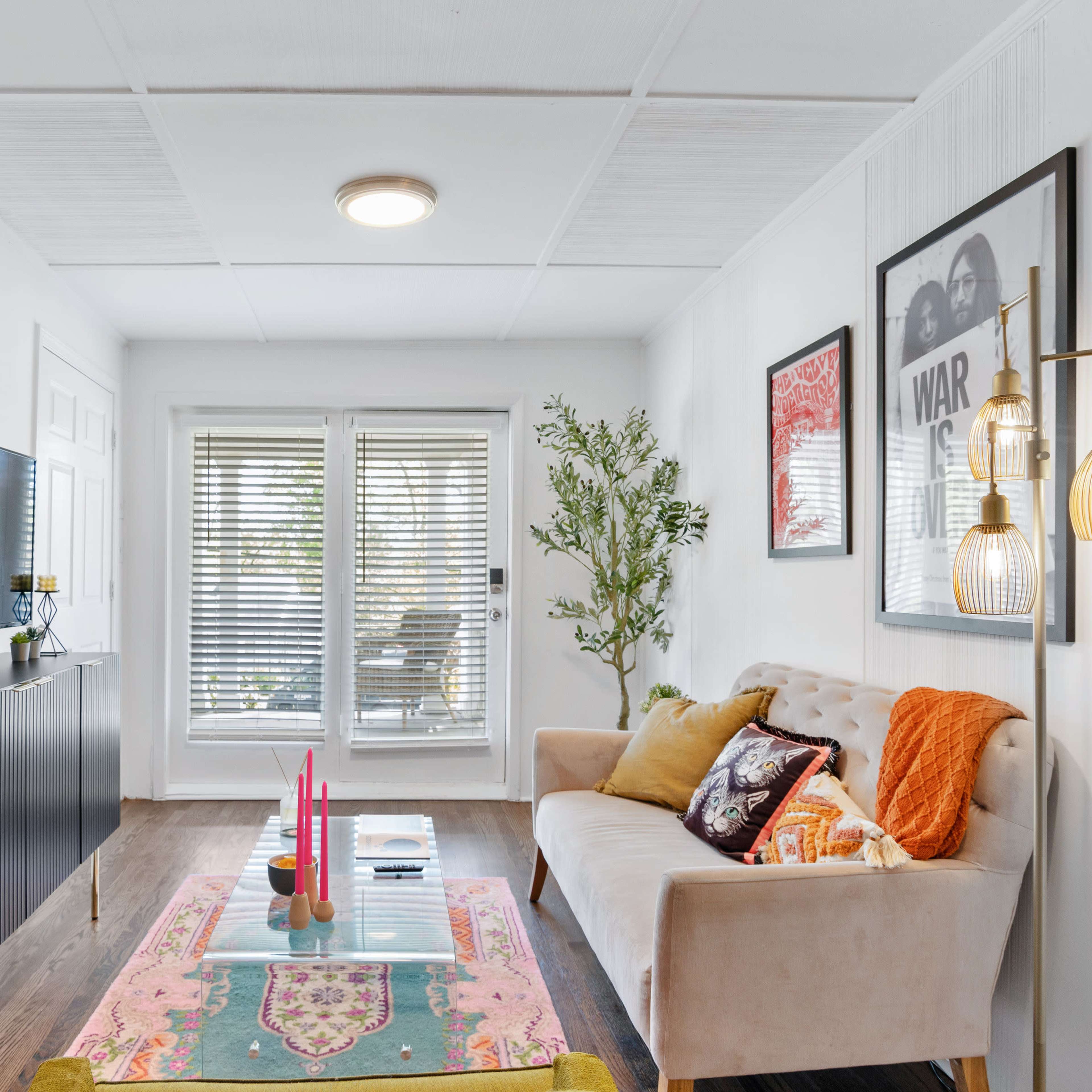 A bright living room featuring a beige sofa, a black television cabinet, a glass coffee table with decorative items, and sliding doors leading to a patio.