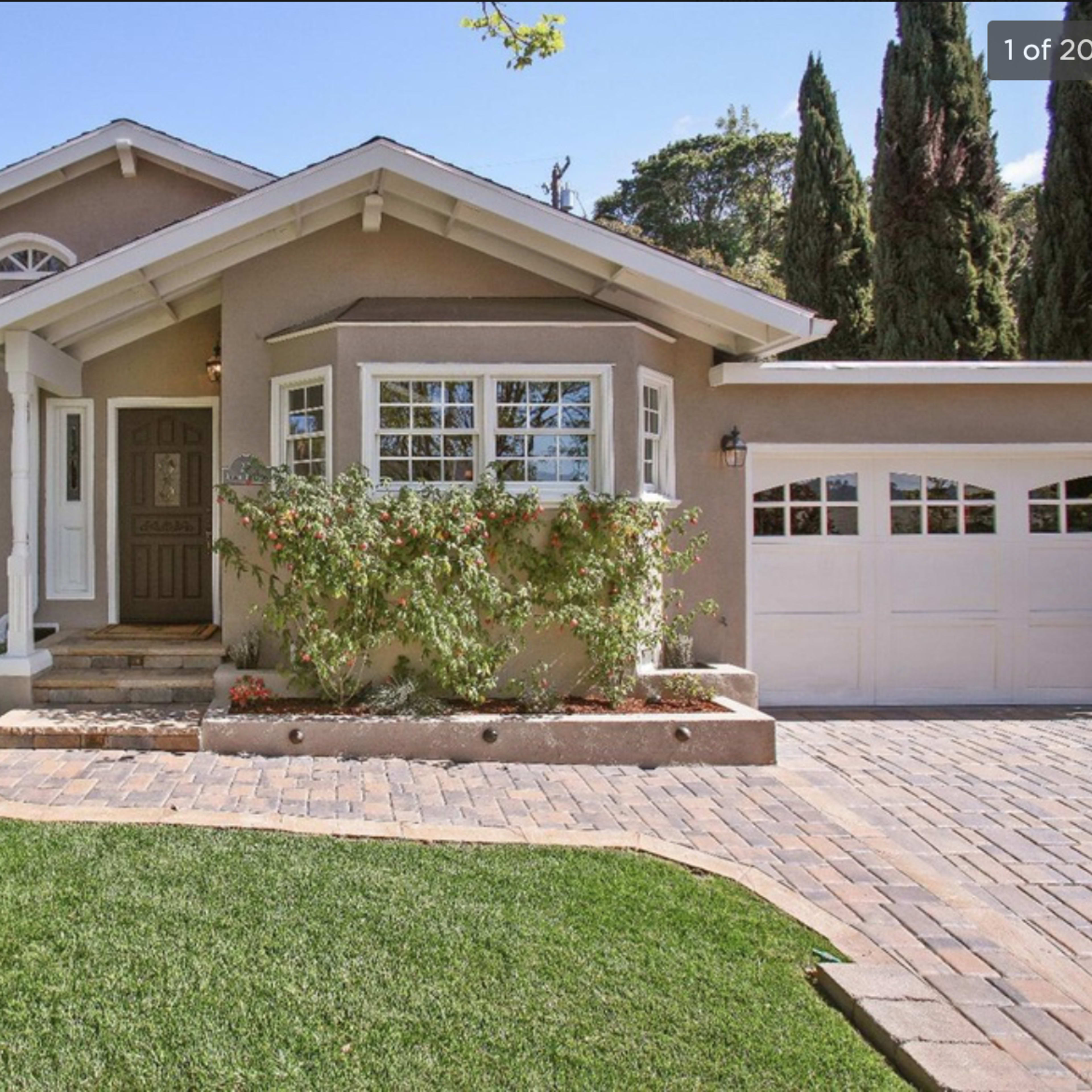 A charming single-story house with beige siding, a small front garden, and a driveway leading to a two-car garage.