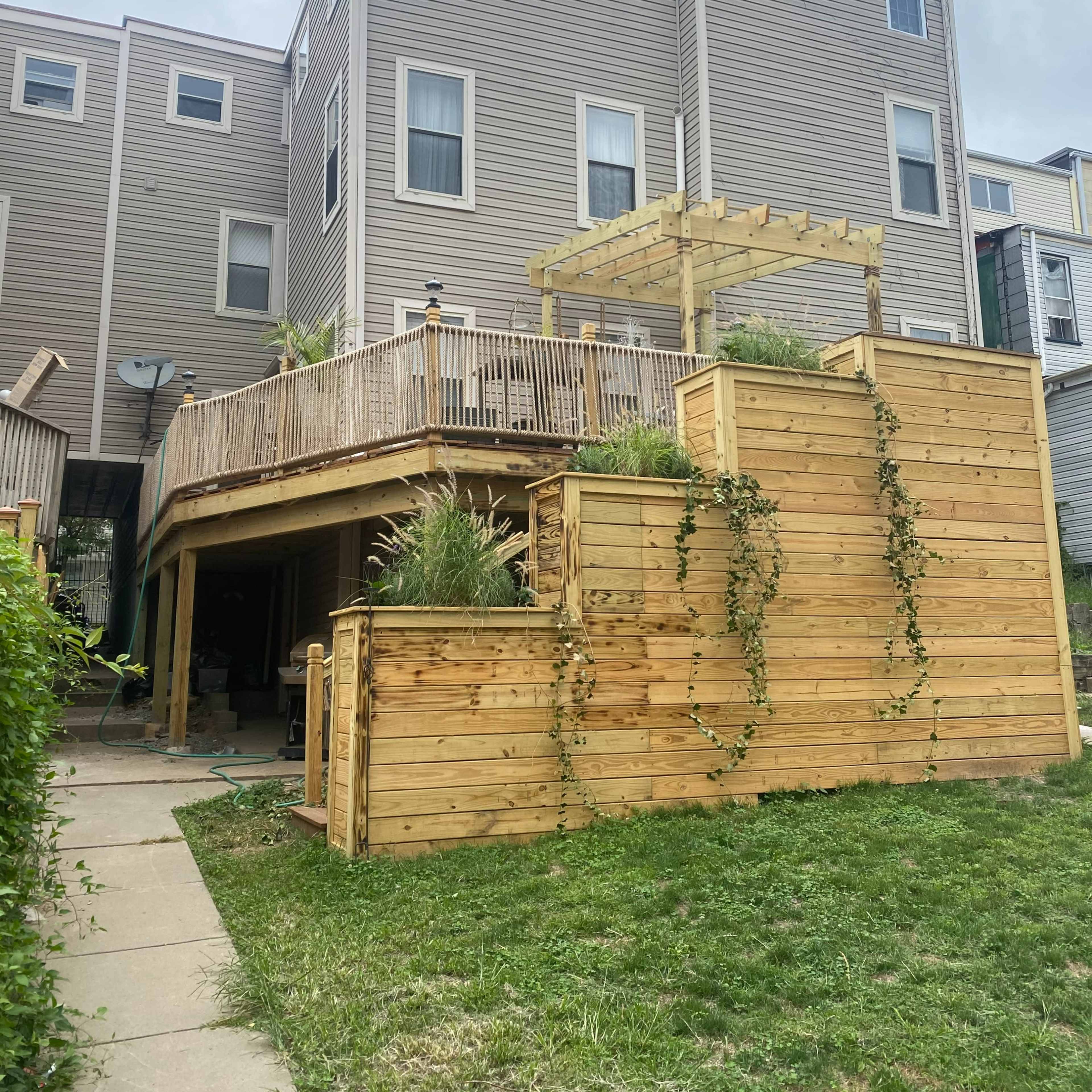 A multi-story building with a wooden deck and a terraced yard featuring wooden retaining walls and greenery.