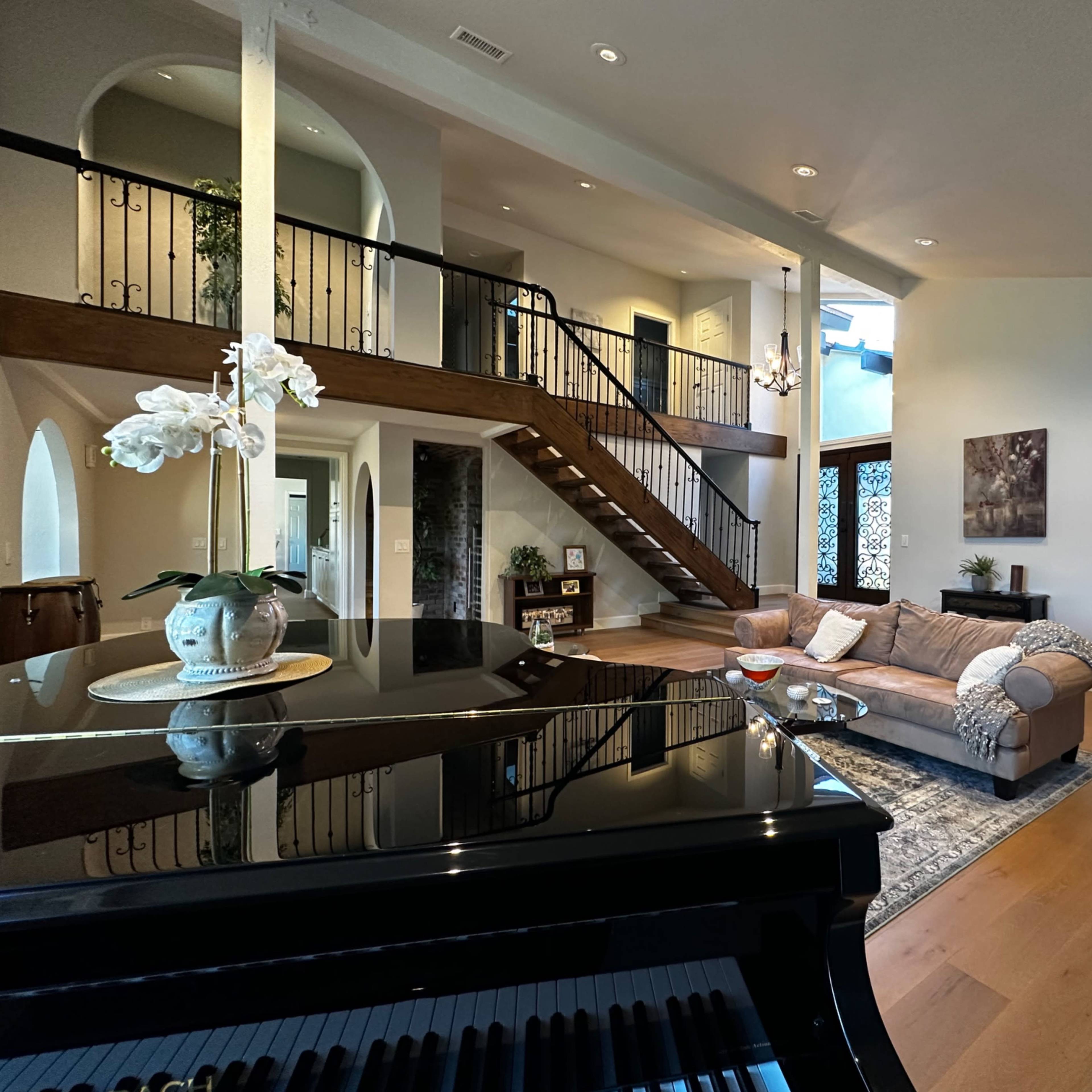 A spacious living room features a grand staircase, ample seating, and a grand piano in the foreground.
