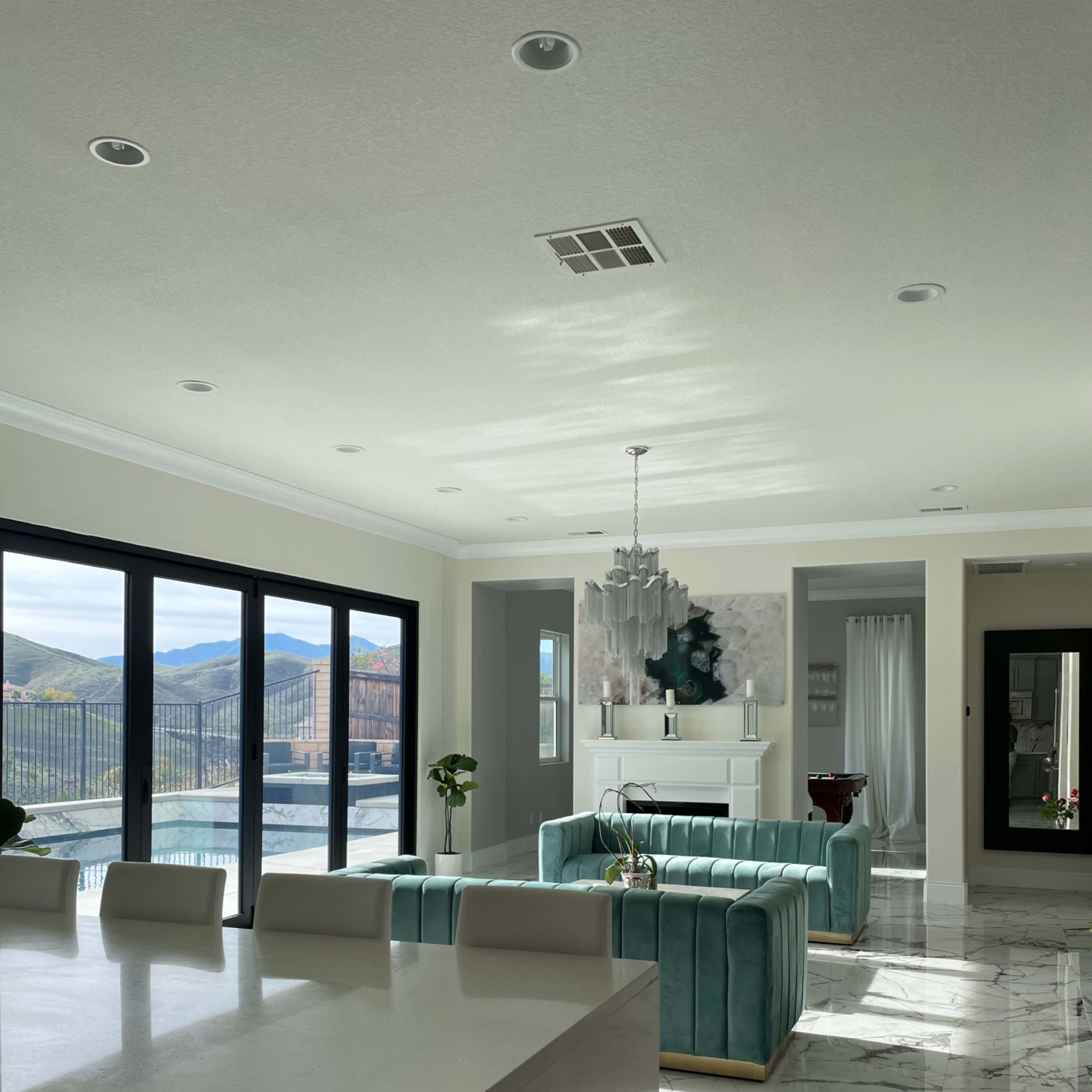 A modern living room with a teal sofa, a marble floor, and large windows displaying a view of mountains.
