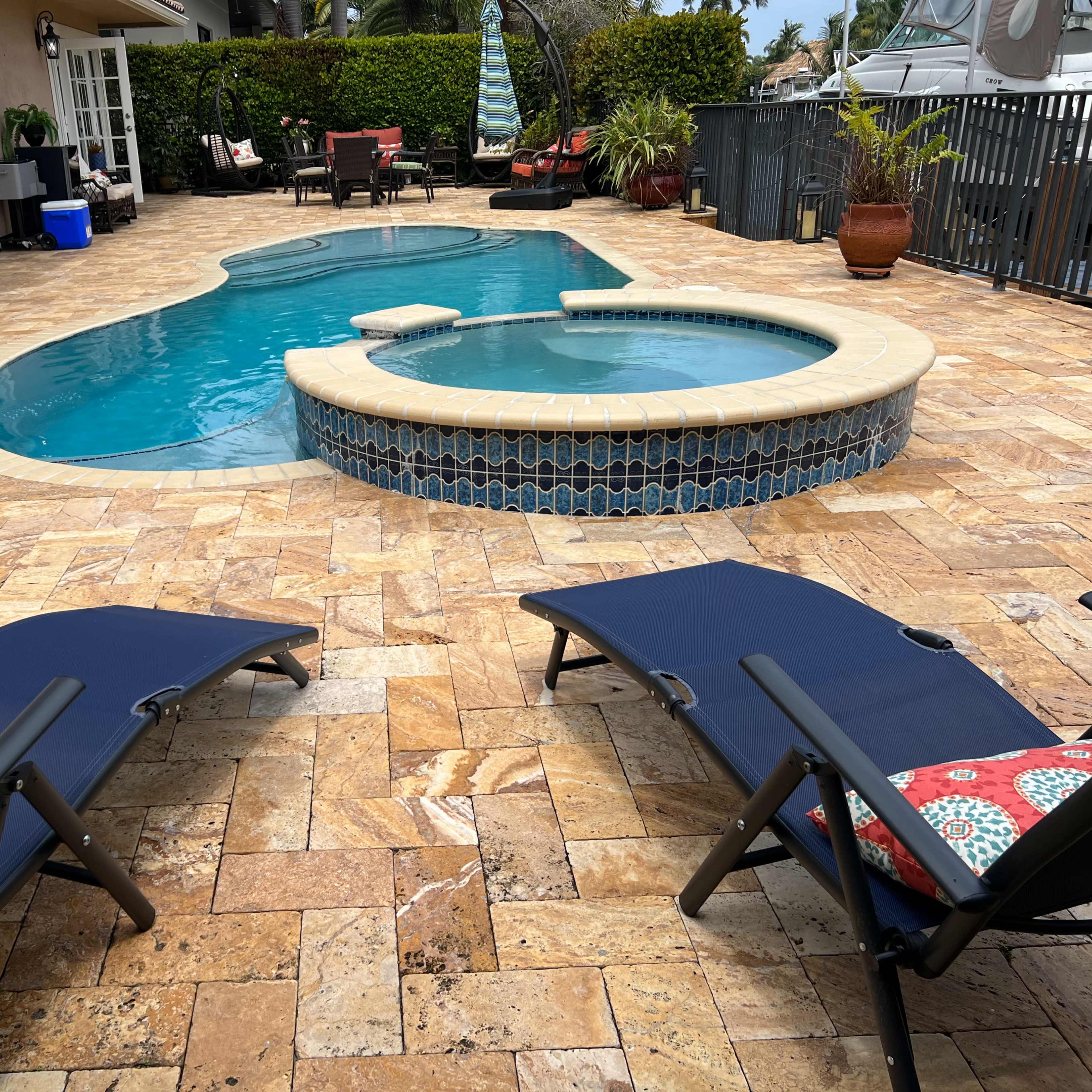 A patio area with a swimming pool and a hot tub, surrounded by lounge chairs and landscaped greenery.