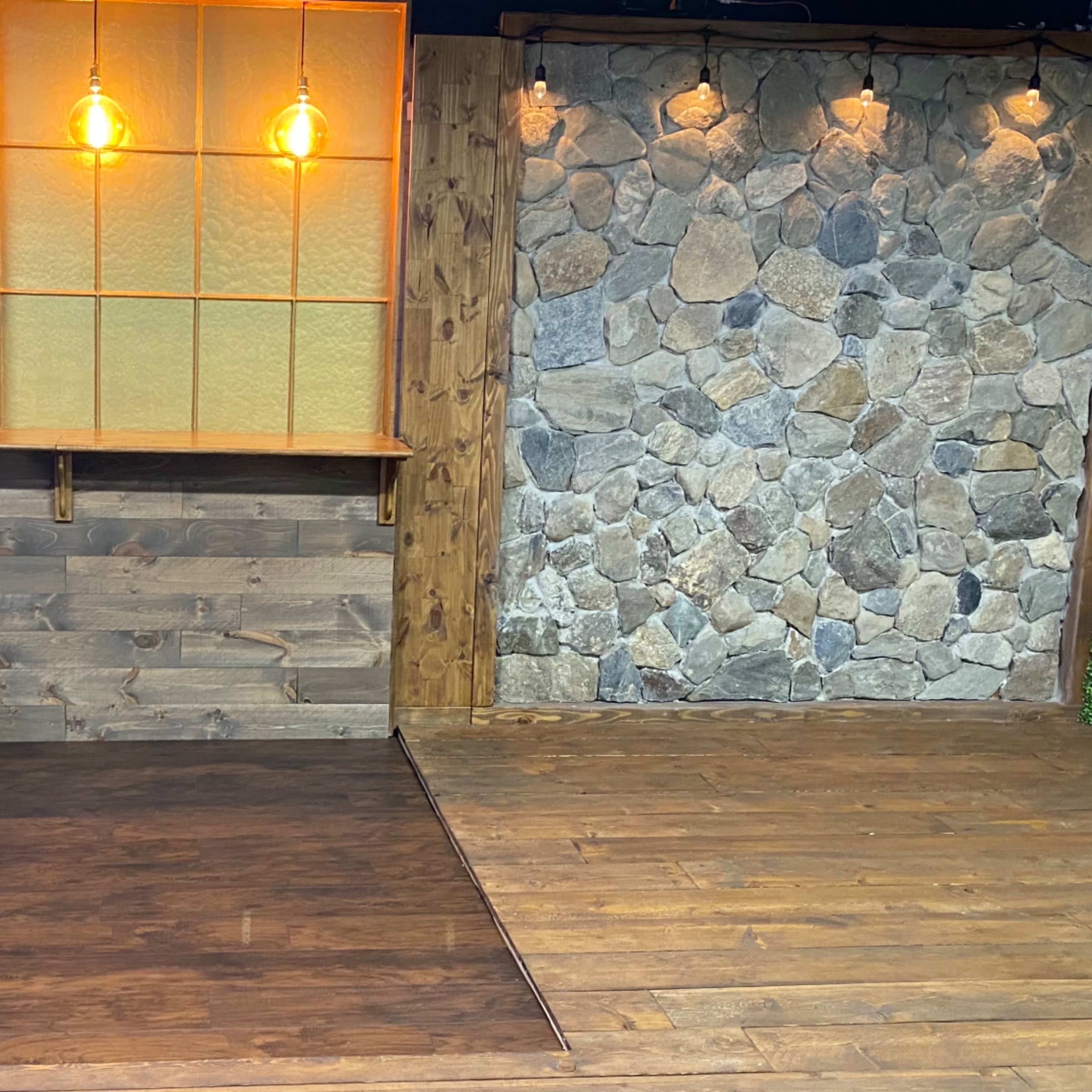 A rustic interior space with wooden panels, a stone wall, and warm pendant lighting.