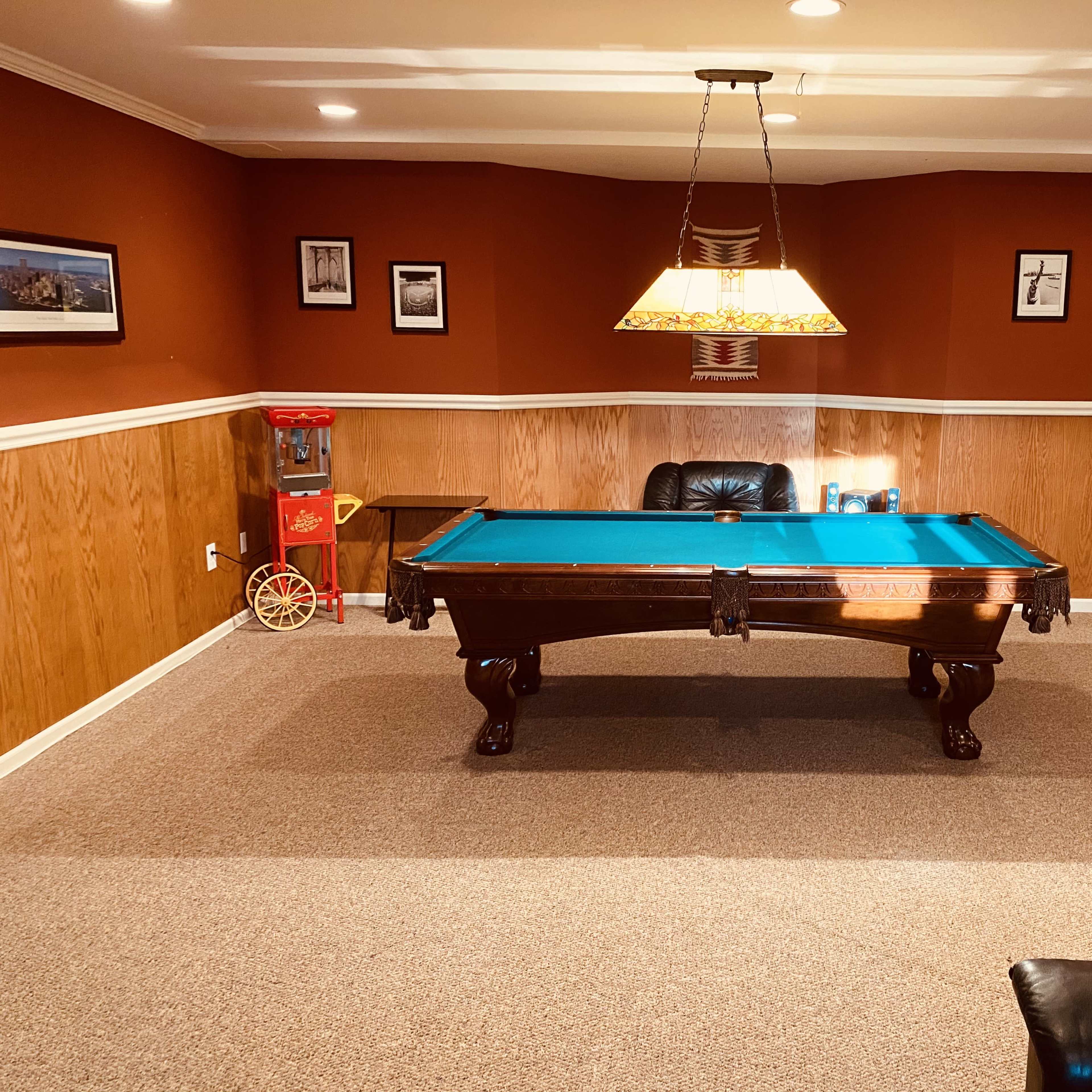 A basement game room featuring a billiards table, a popcorn machine, and framed photographs on the walls.